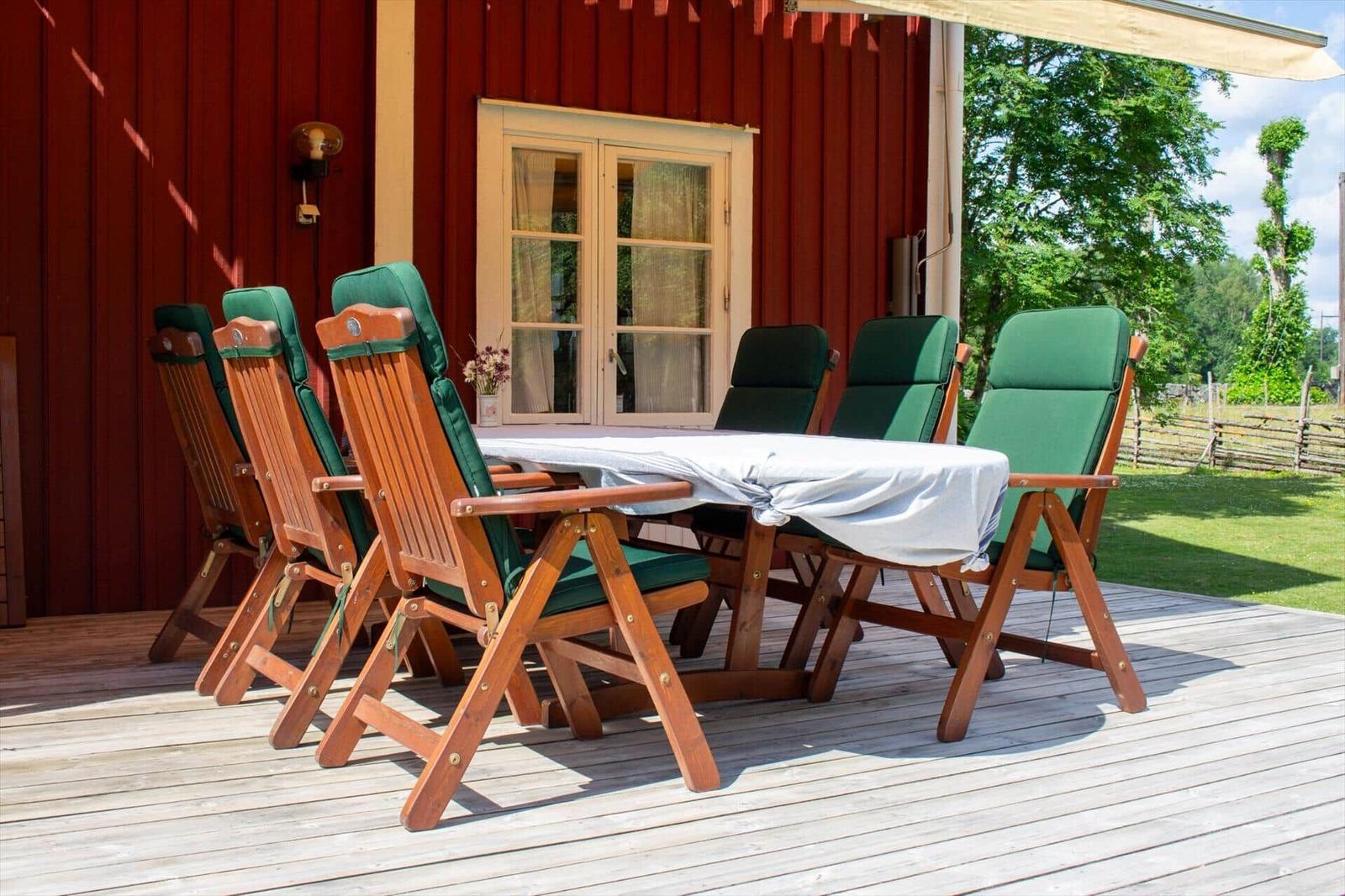 Terrasse mit Holztisch und grünen Stühlen vor rotem Holzhaus.