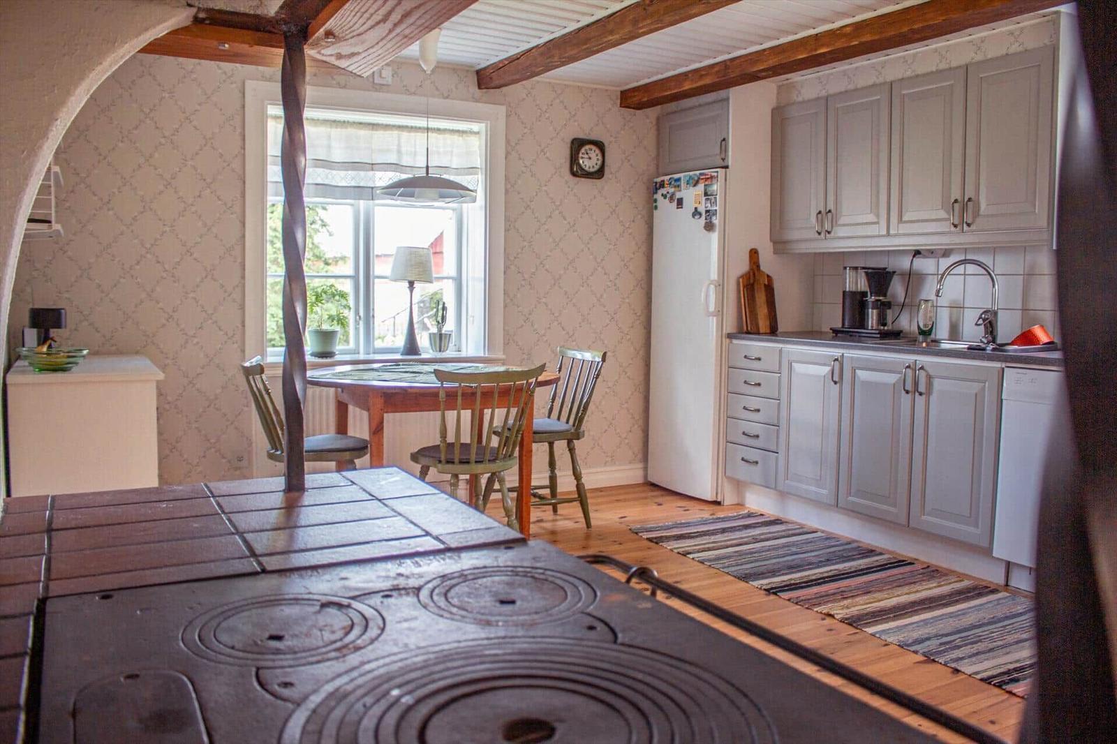 Küche mit Essbereich, Holzboden und Küchenschränken. Fenster mit Lampe und Tisch mit Stühlen.