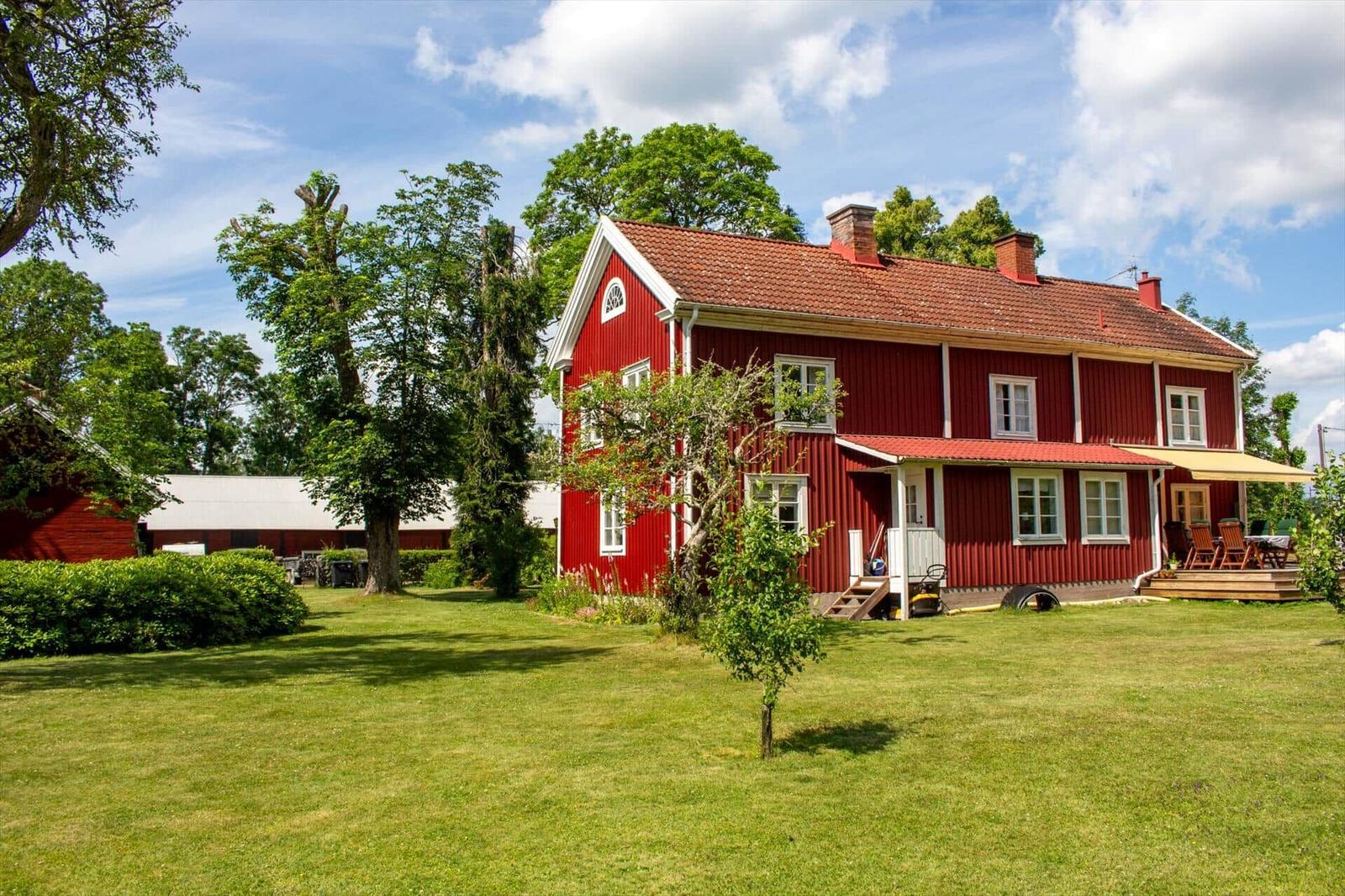 Rotes Holzhaus mit Terrasse und Garten unter blauem Himmel.