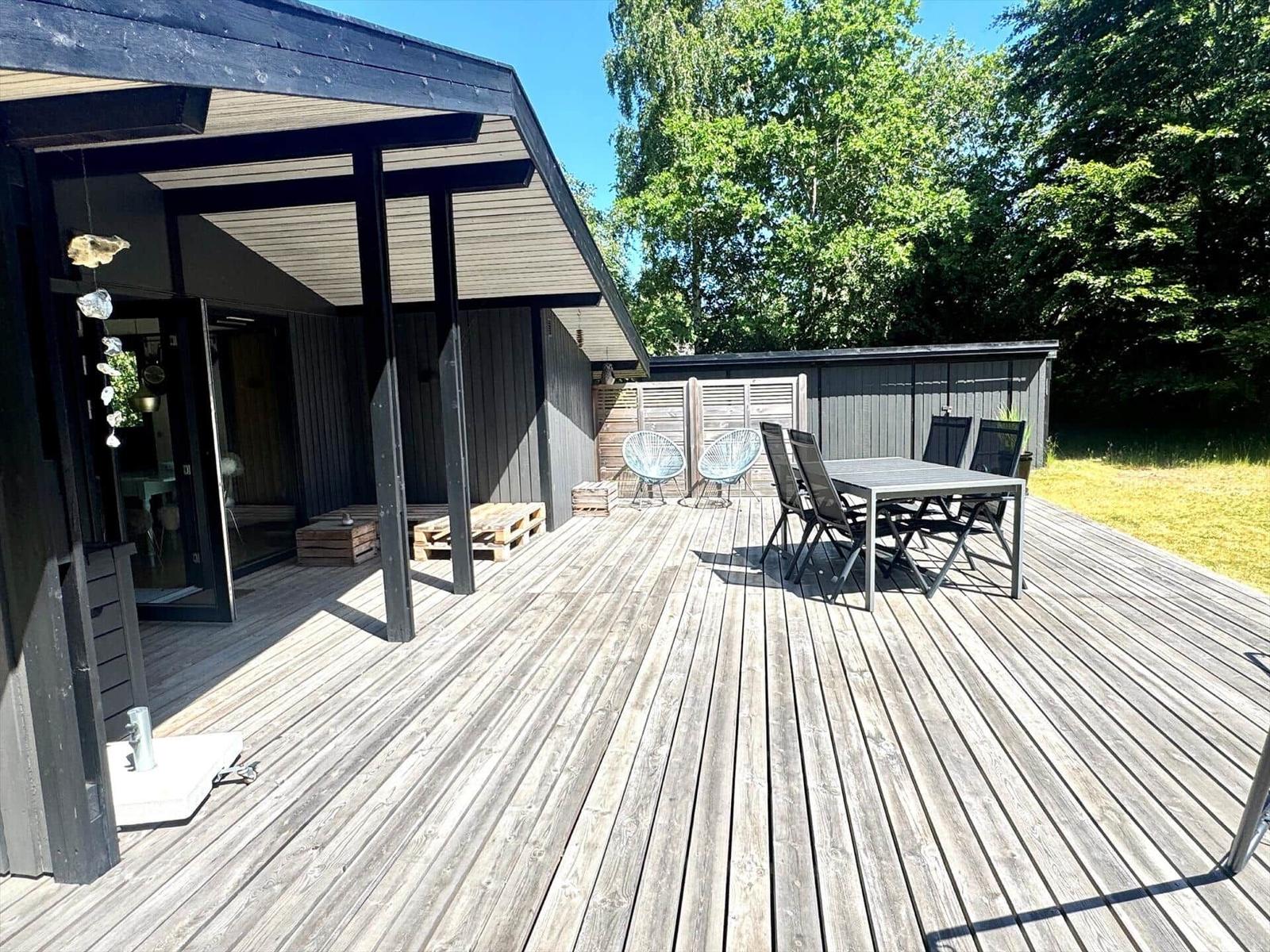 Terrasse mit Tisch, Stühlen und Pavillon. Hinterhof mit Holzhaus und Bäumen.