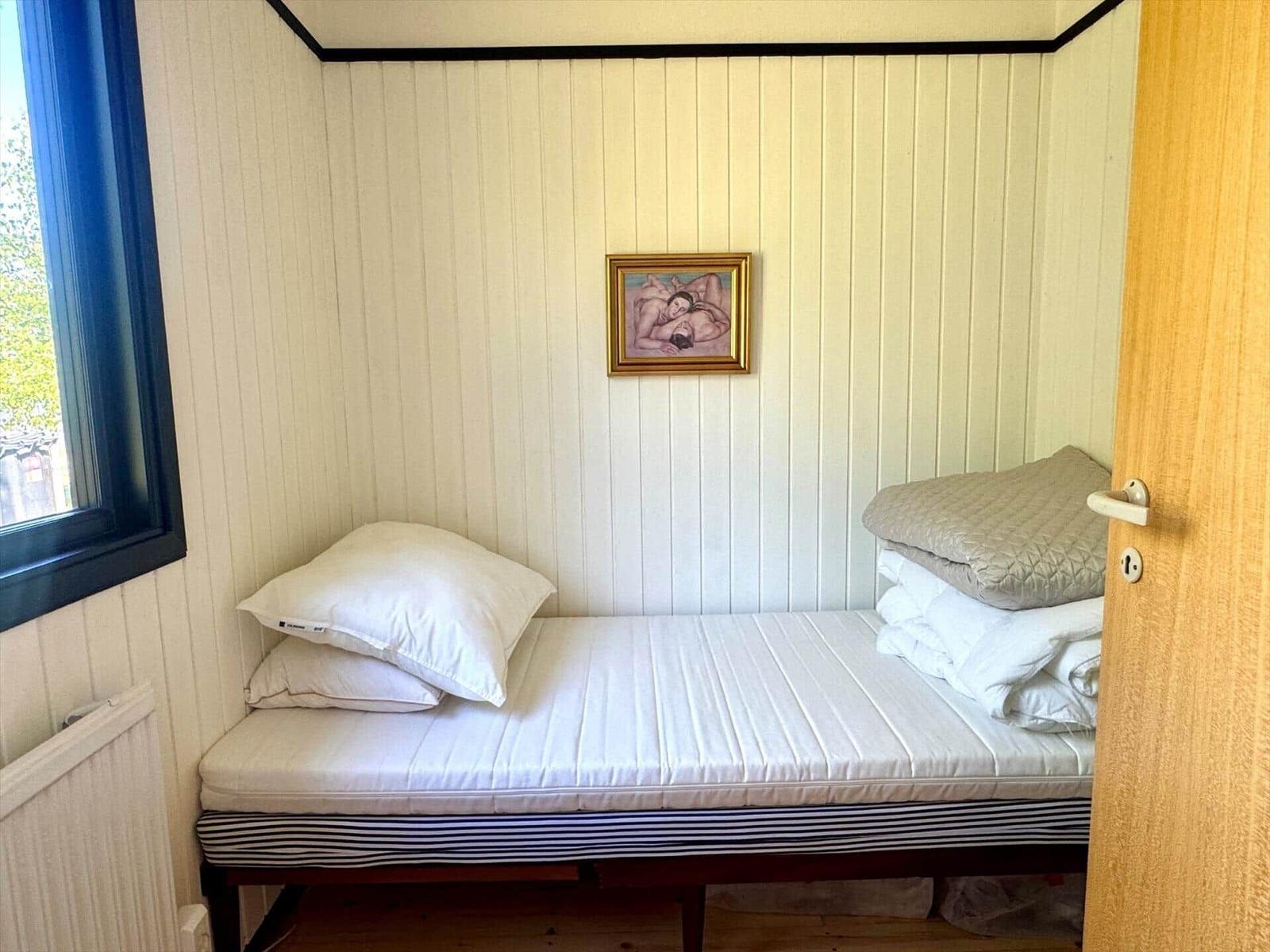 Ein Bett mit Kissen und Bettwäsche in einem Raum mit vertikal verkleideten Wänden und einem Fenster.