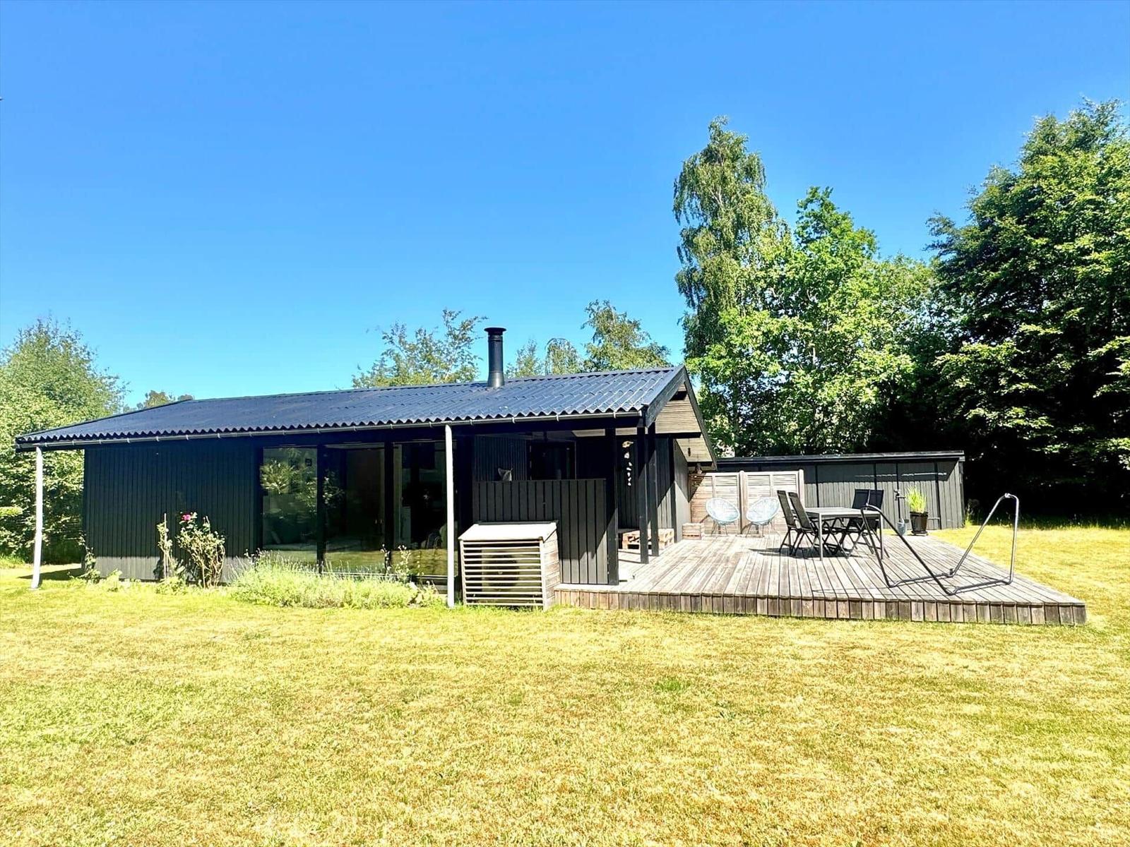 Moderne Hütte mit Terrasse, Garten und Grillplatz unter blauem Himmel.