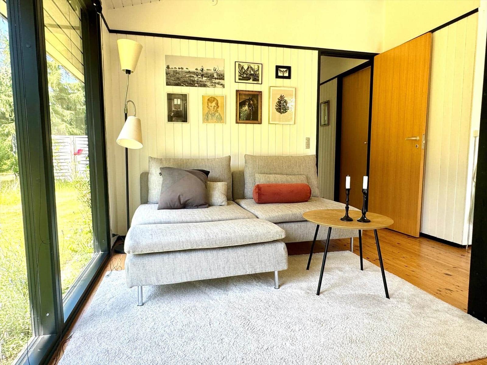 Ein Wohnzimmer mit Sofa, Tisch und Wanddekoration. Große Fenster und Holzboden.