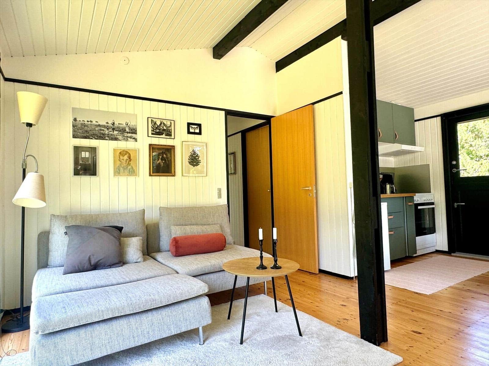 Wohnzimmer mit Sofa, Tisch und Wandbildern. Küche im Hintergrund sichtbar.
