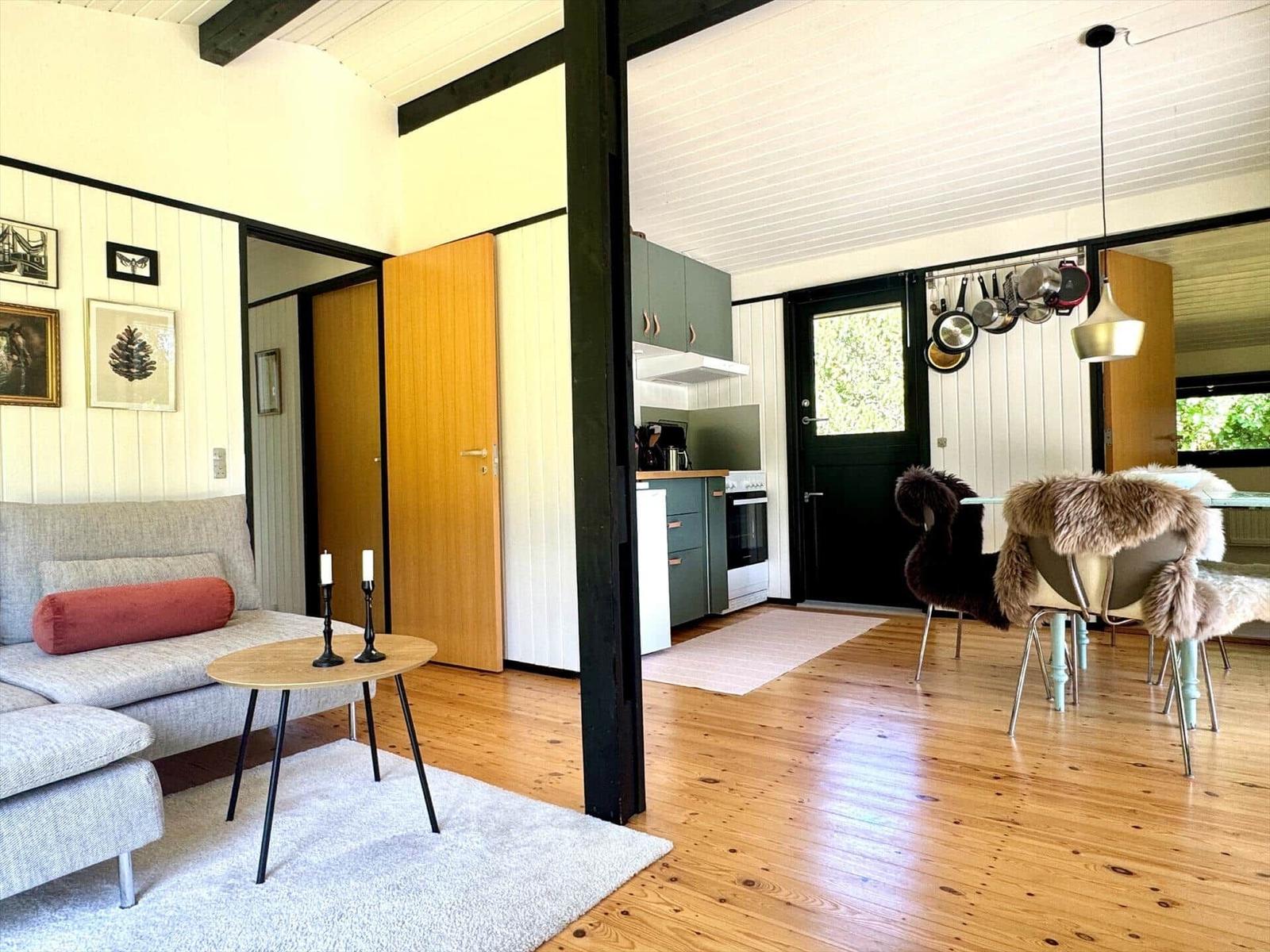 Wohn- und Essbereich mit Küche. Holzboden, Sofa, Tisch und Stühle mit Felldecken.