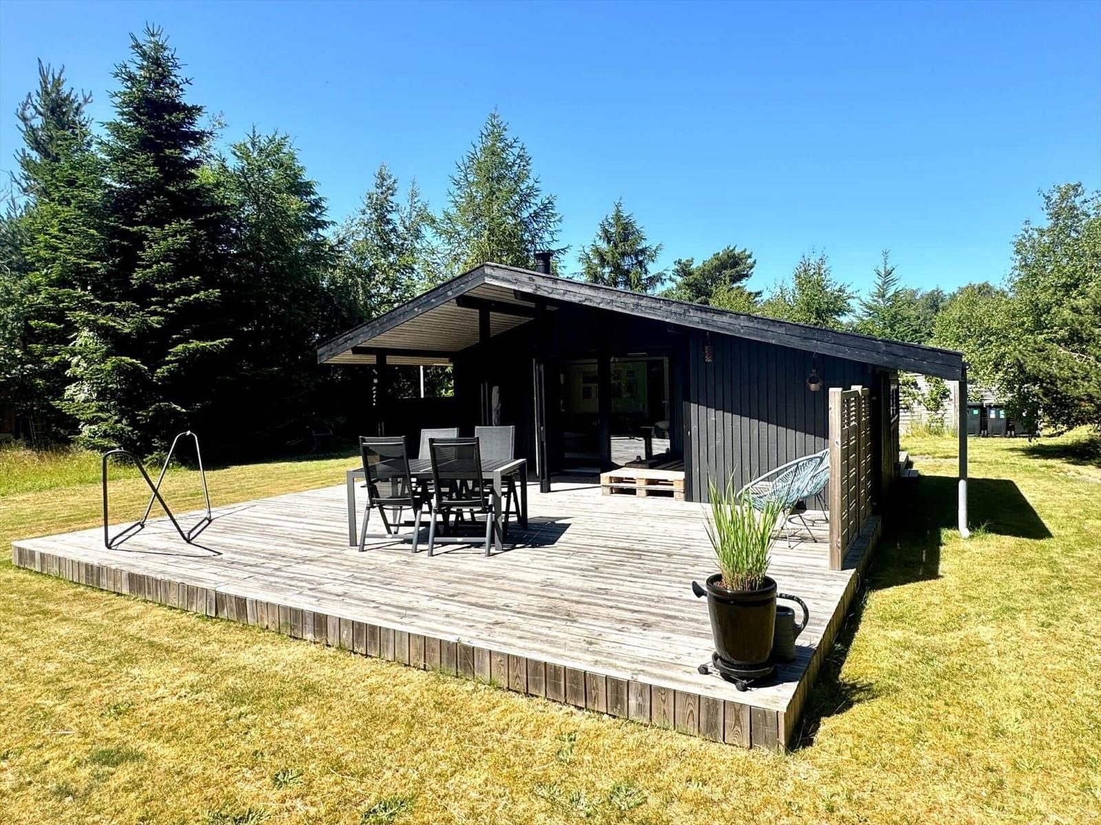 Holzterrasse mit Tisch, Stühlen und Pflanze vor einem Haus mit Schuppen