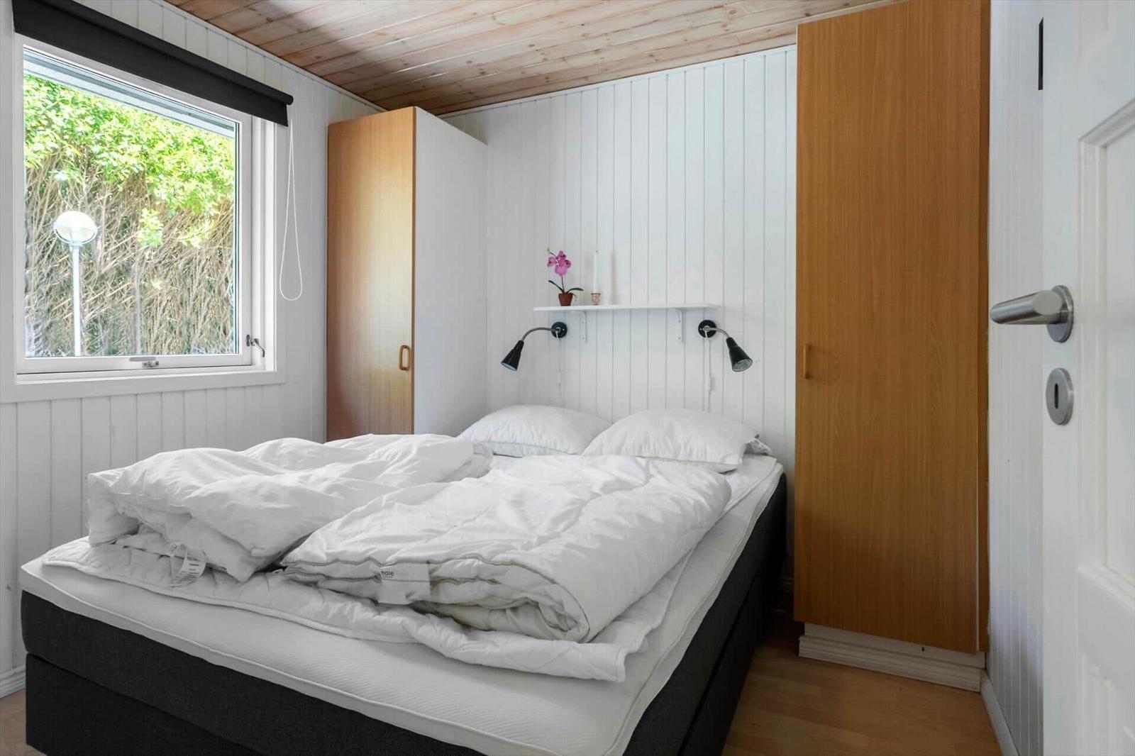 Schlafzimmer mit Bett, Fenster und Holzmöbeln.