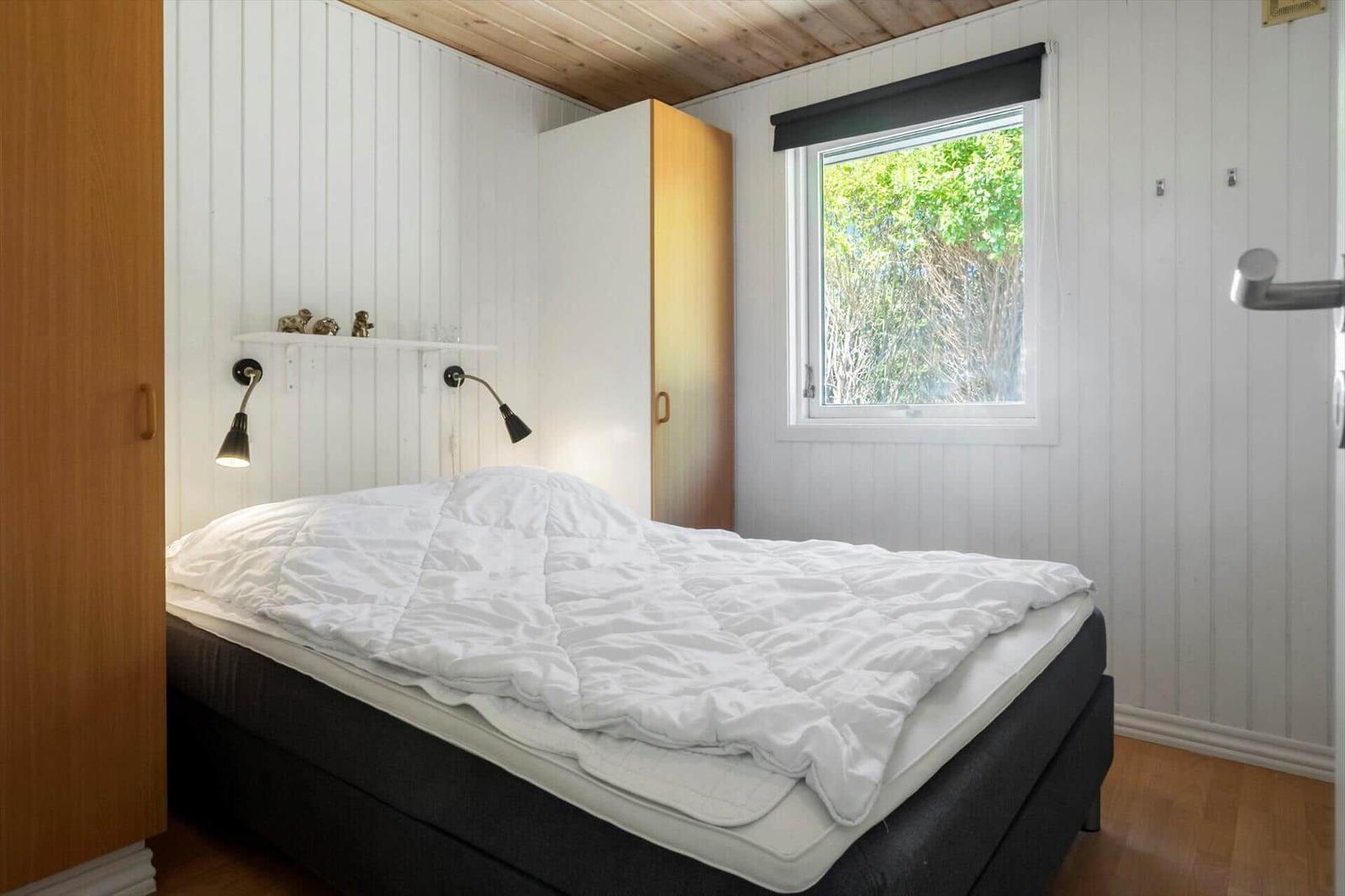 Schlafzimmer mit Bett, Fenster und Holzwandverkleidung.