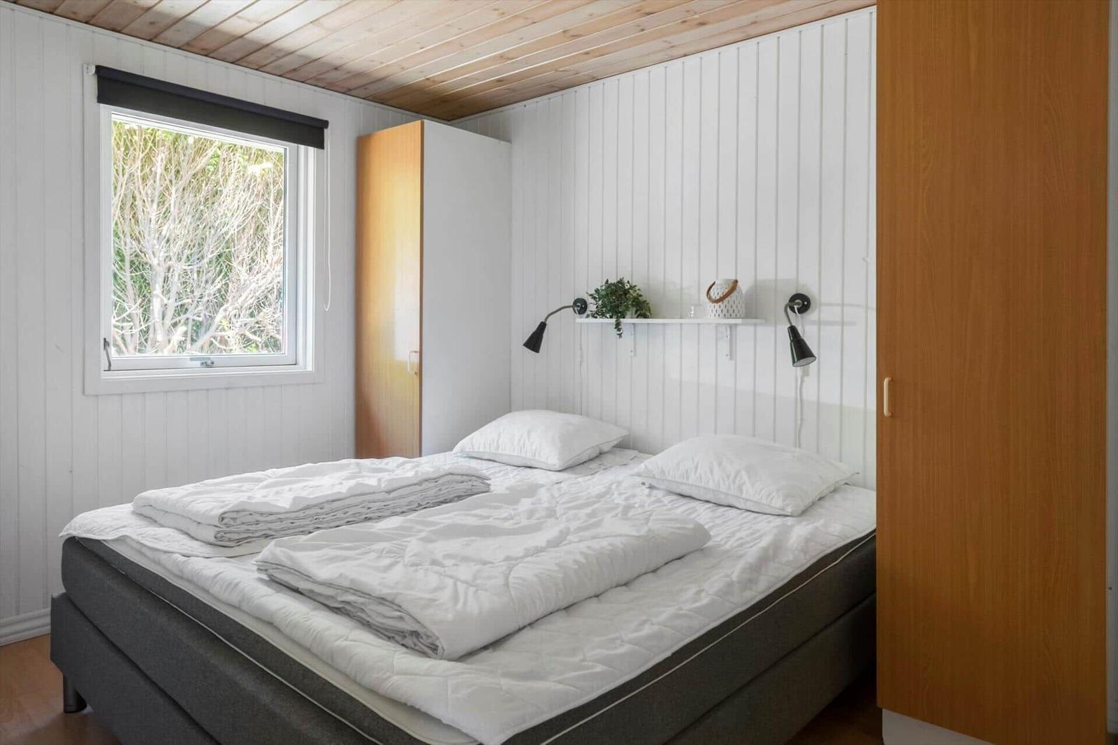 Schlafzimmer mit Bett, Fenster und Schrank. Wand mit Regal und Lampen.