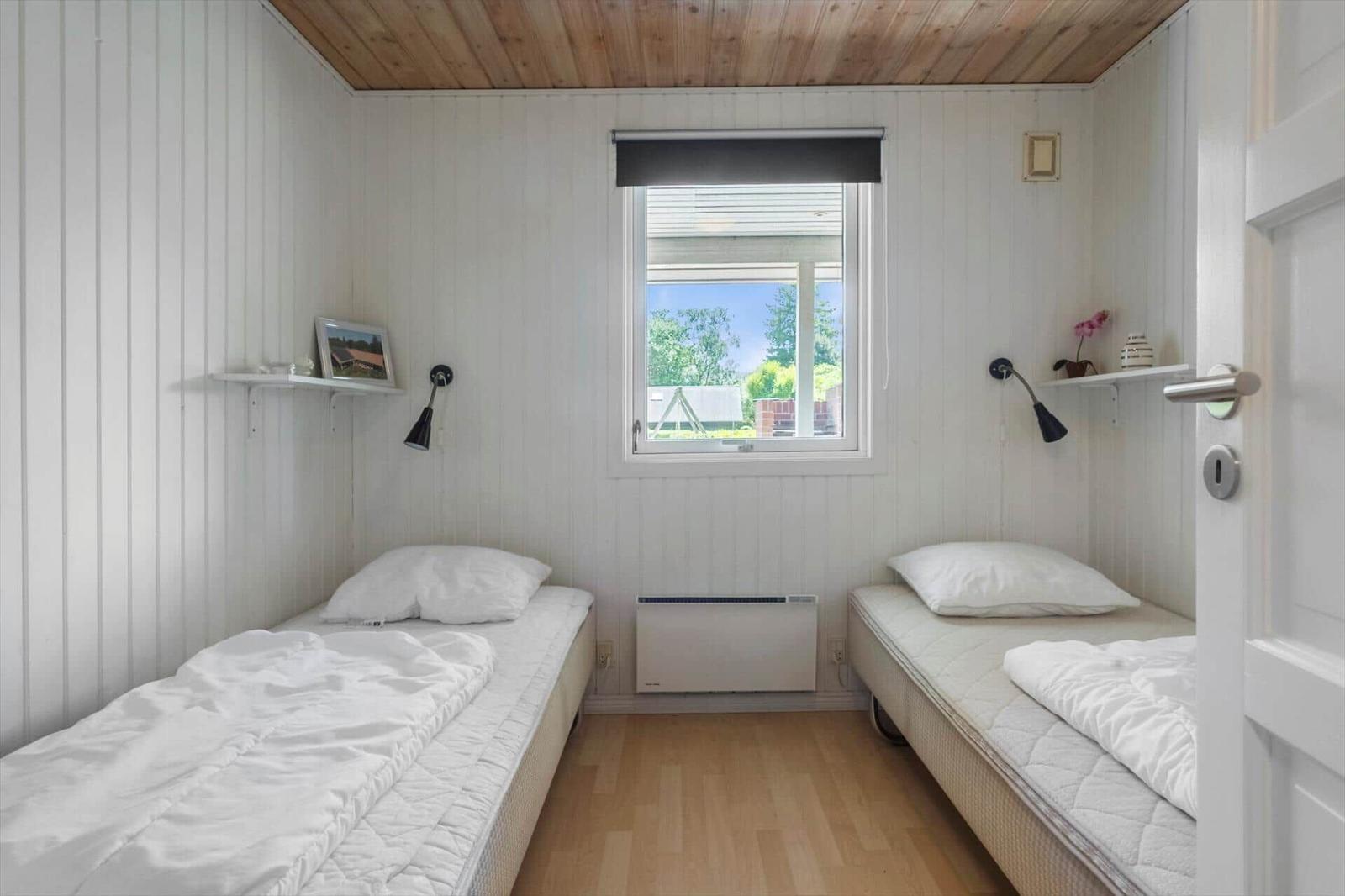 Zwei Einzelbetten mit weißen Laken stehen in einem Raum mit Holzfußboden und weißem Paneelwandverkleidung.