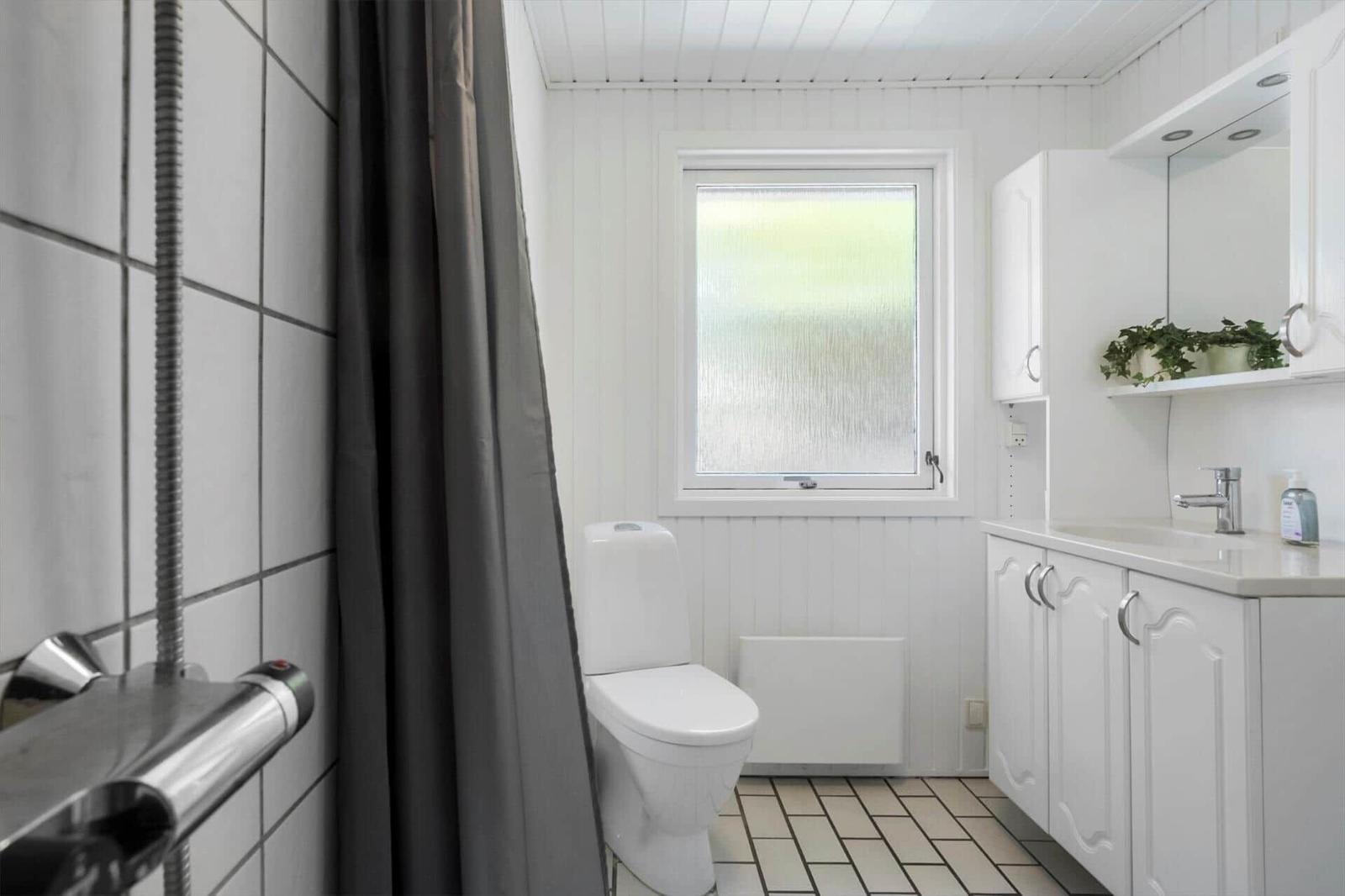 Badezimmer mit Toilette, Waschbecken und Dusche. Fenster mit getöntem Glas.