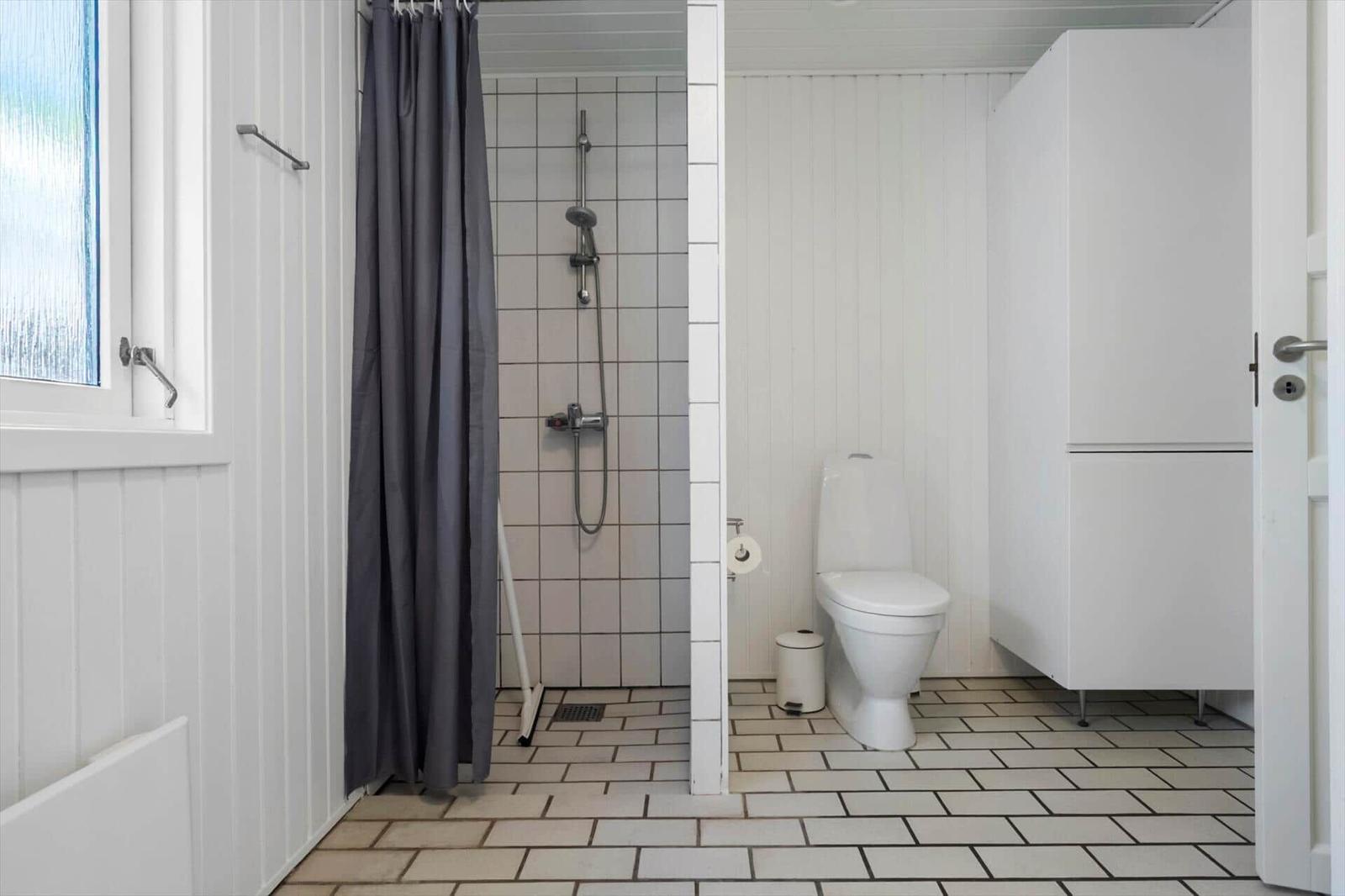 Badezimmer mit Dusche, Toilette und Fenster. Weiße Wände und Fliesen.