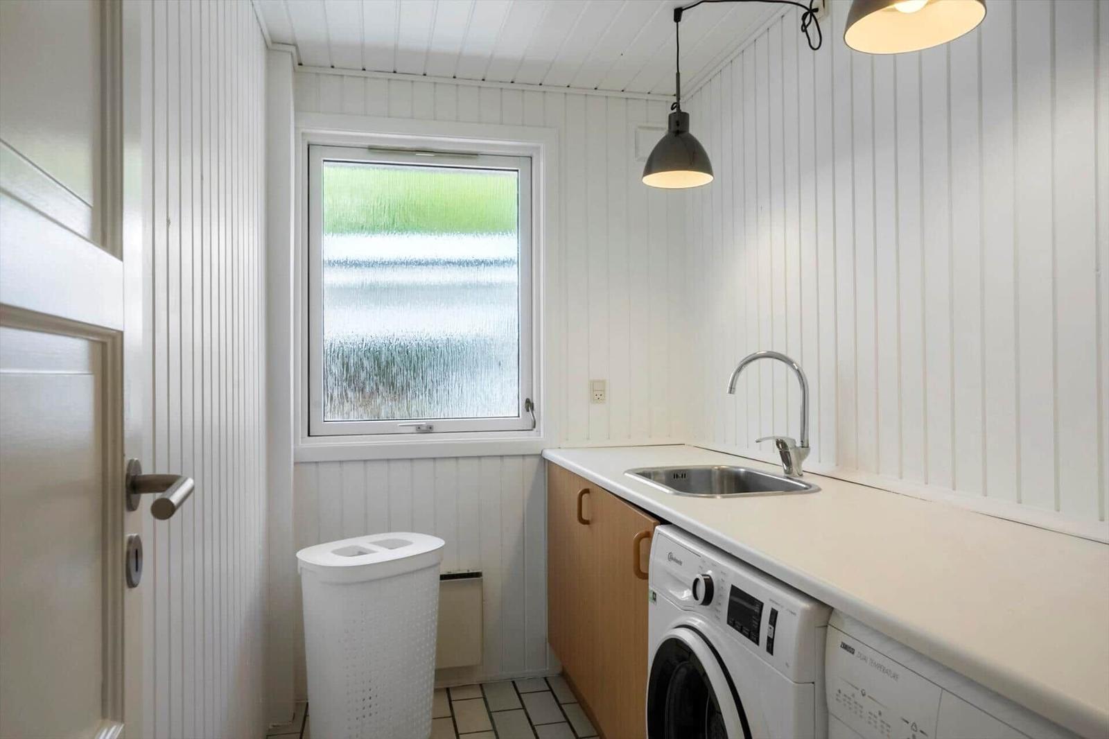 Wohnraum mit Waschmaschine, Spüle und Fenster. Weiße Wände und Holzschränke.