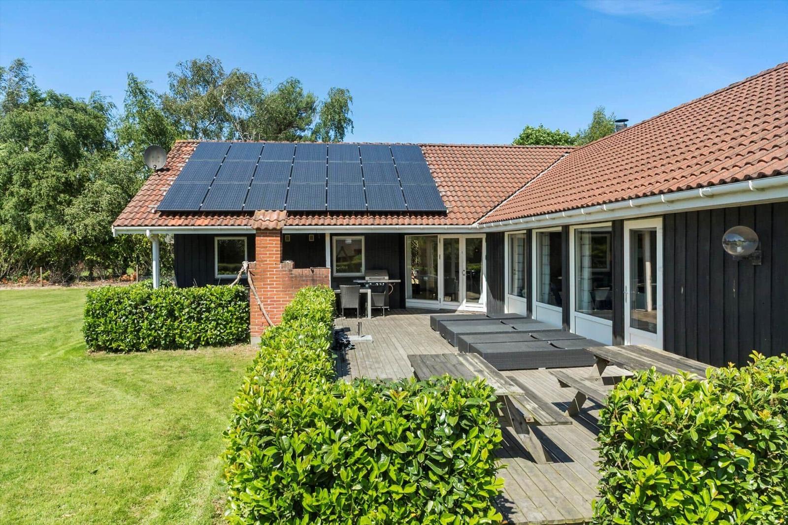 Haus mit Solaranlage, Terrasse und Garten. Holzterrasse mit Liegen und Grill.