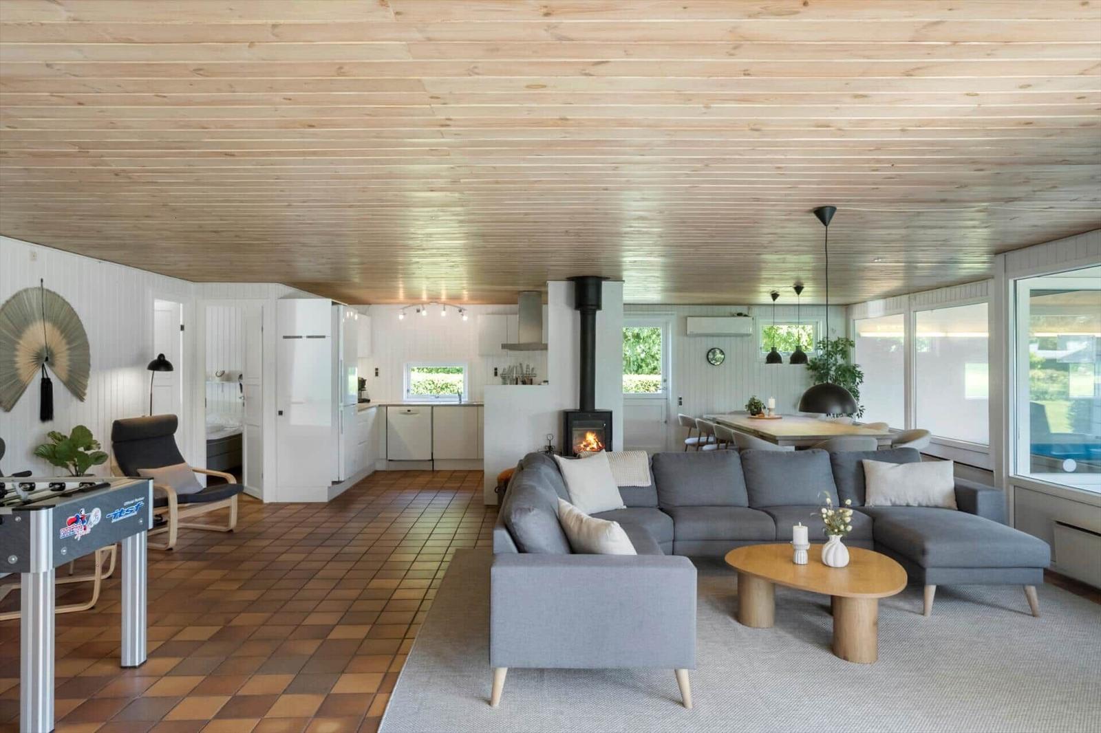 Wohnzimmer mit Kamin, Sofa und Küchenbereich unter Holzdecke.