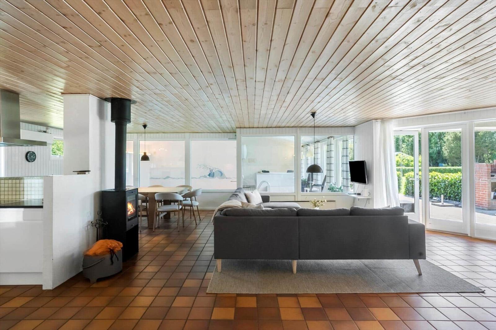 Wohnzimmer mit Sofa, Kamin und Terrassentür. Holzdecke und Fliesenboden.