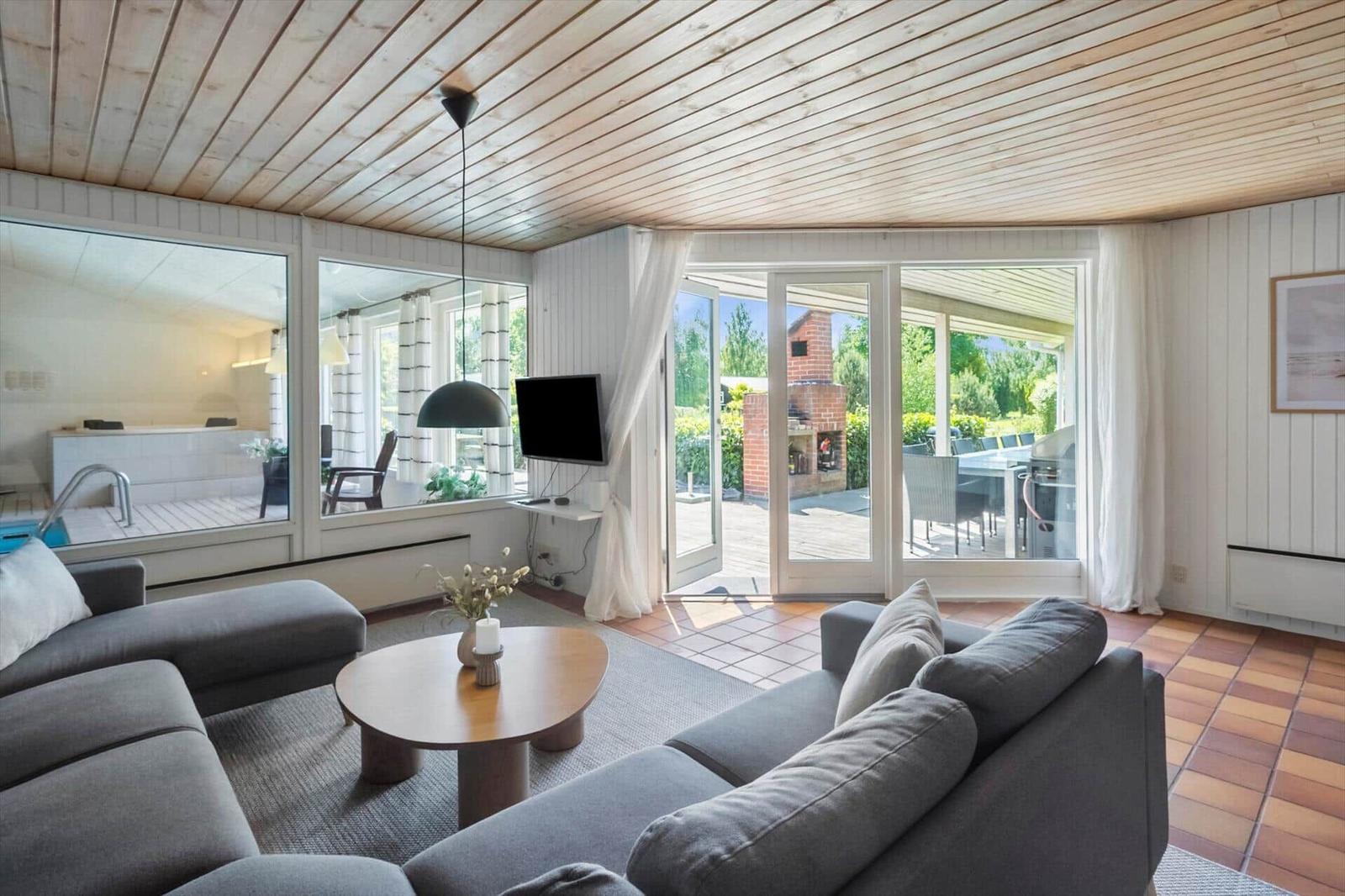 Wohnbereich mit Sofa, Couchtisch und TV. Durchgänge zu Terrasse und Bad.