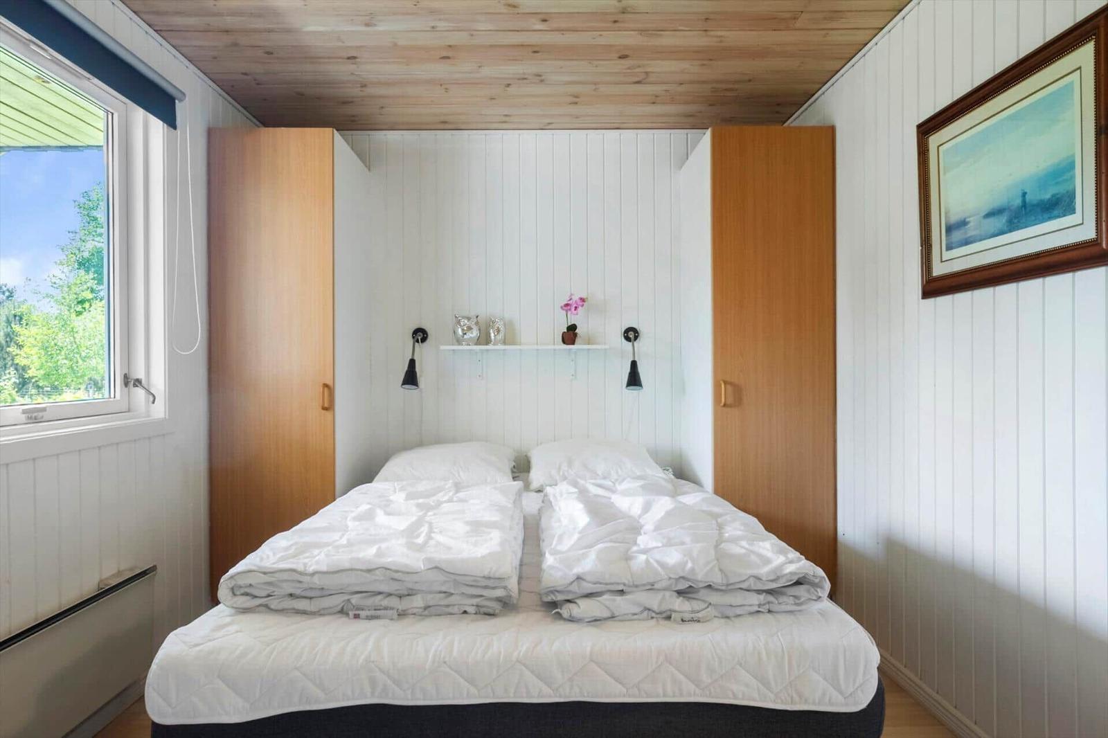 Schlafzimmer mit Doppelbett, Holzdecke und Fenster mit Blick auf Grün.