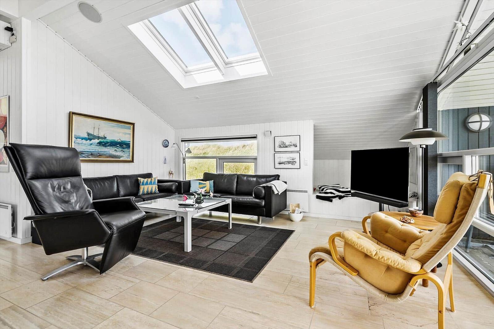 Wohnzimmer mit schwarzen Ledermöbeln, Holzboden und Dachfenstern. Gelber Sessel und Fernseher sichtbar.