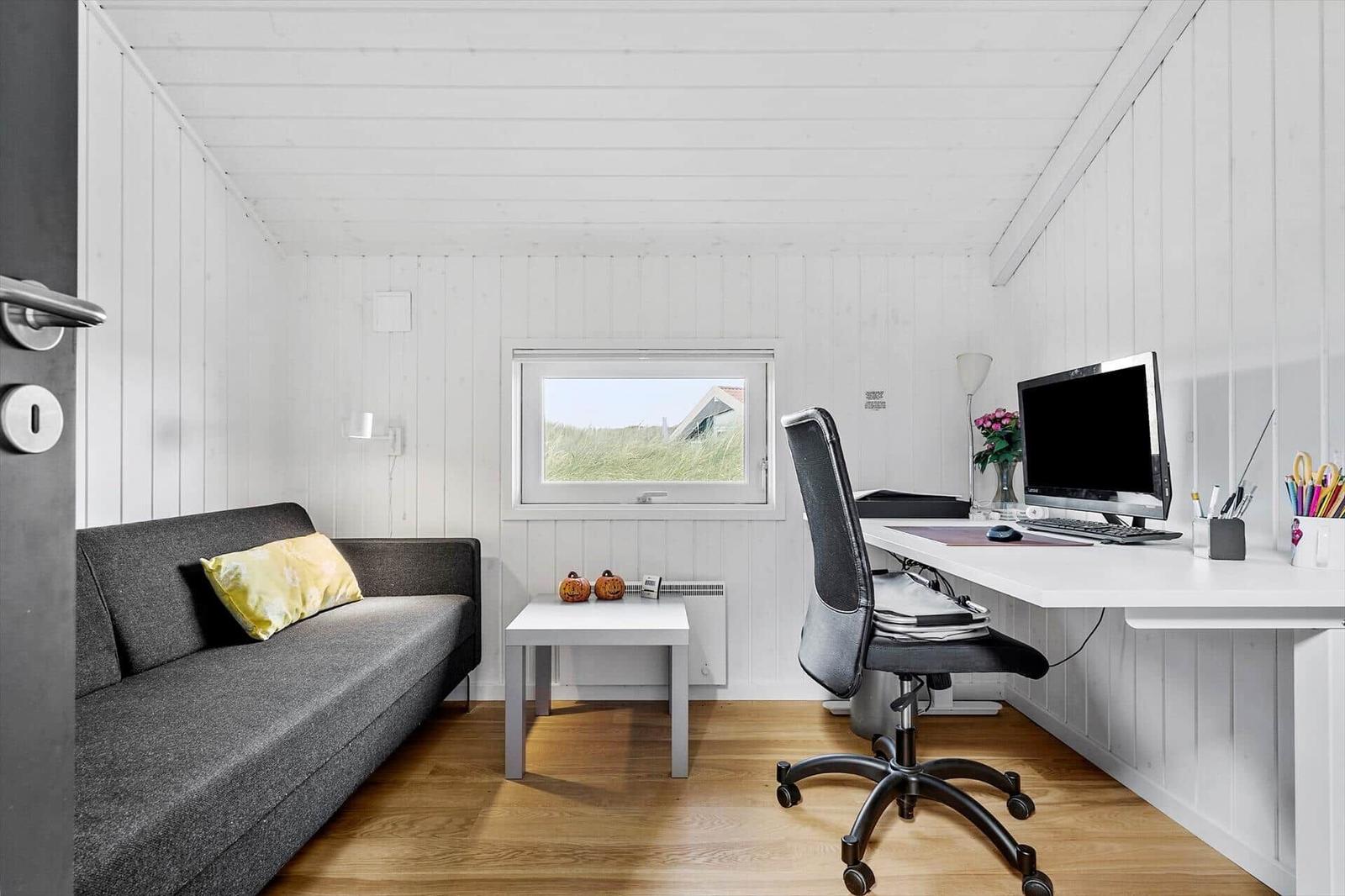 Ein Raum mit Sofa, Schreibtisch und Fenster mit Blick auf Gras.