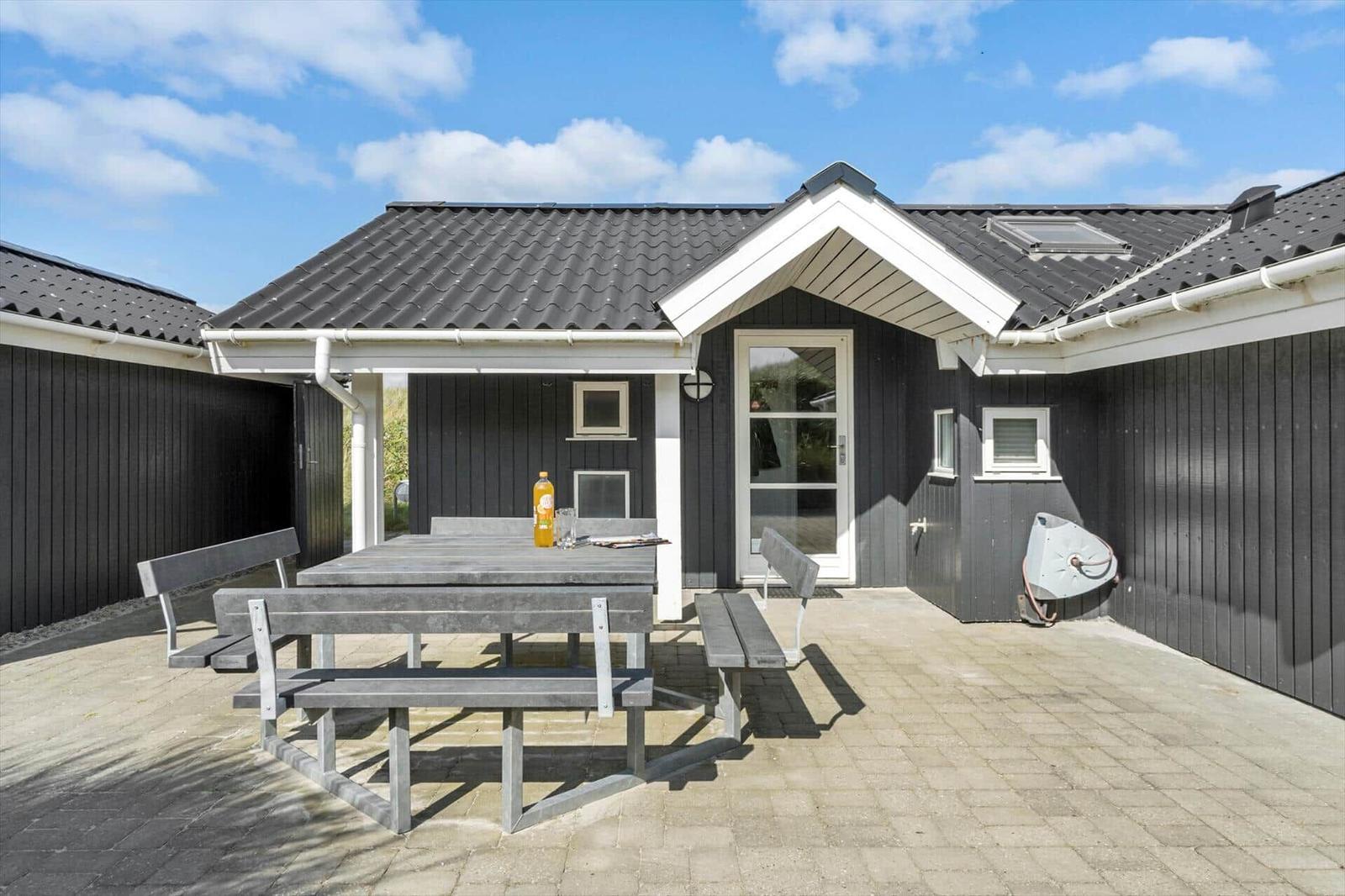 Haus mit Terrasse, Tisch und Bänken. Schwarze Fassade, weißer Rahmen und Dach.