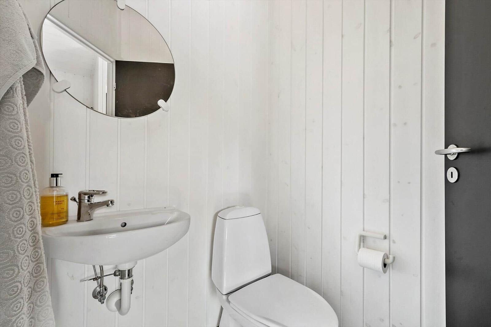 Badezimmer mit Waschbecken, Toilette und runden Spiegel an weißen Holzwänden.