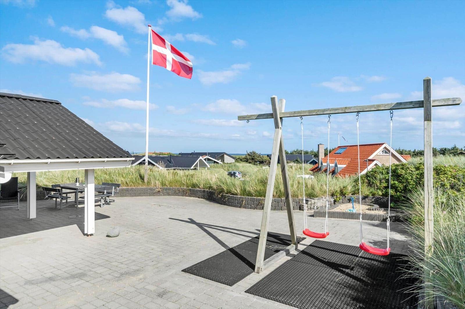 Terrasse mit Schaukel, Tisch und dänischer Flagge. Hintergrund: Gras und Häuser.