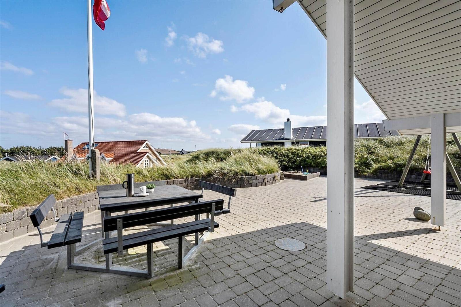 Terrasse mit Tisch und Bänken, Blick auf Strand und Häuser.
