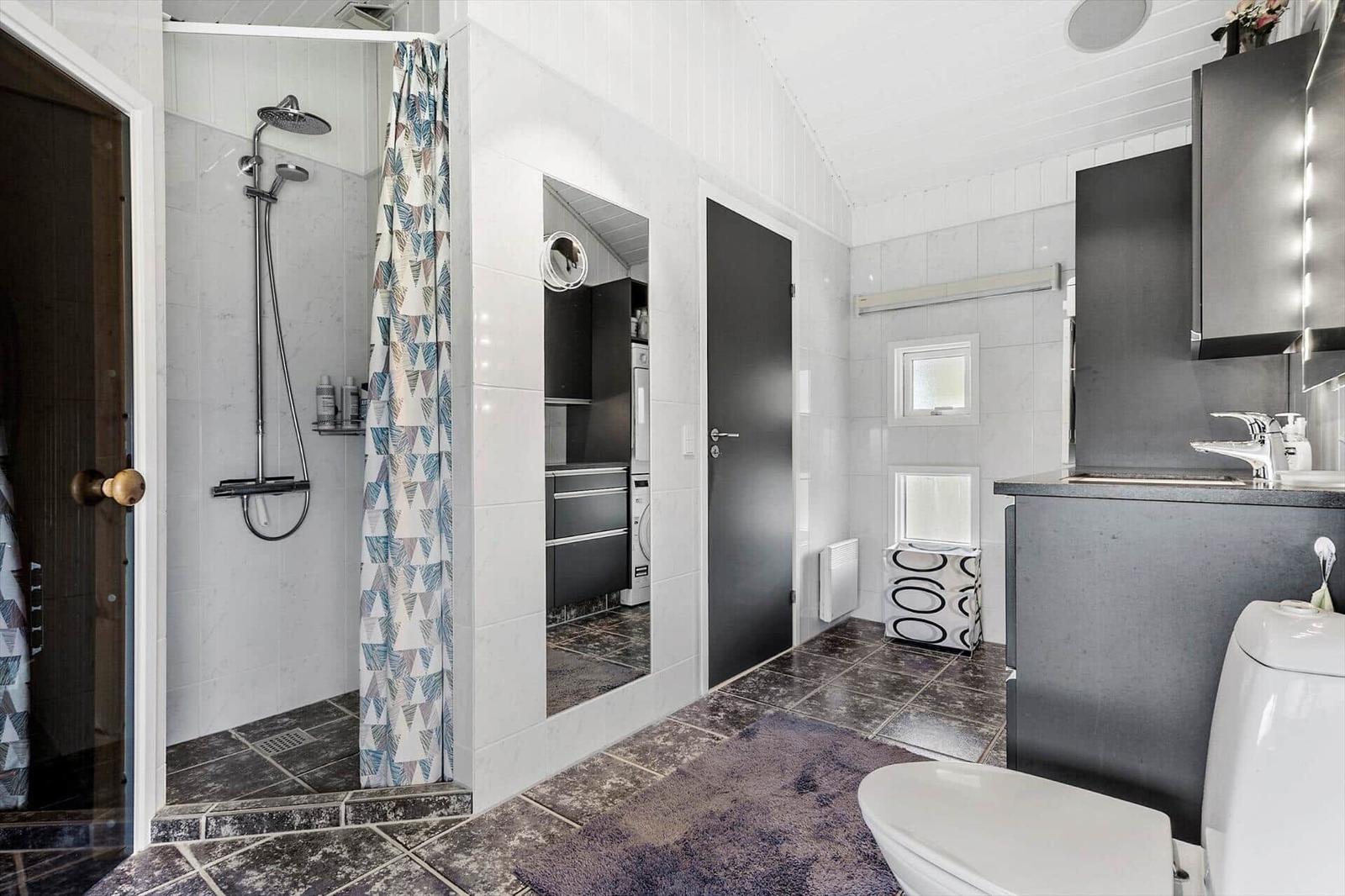 Badezimmer mit Dusche, Toilette und Waschbecken. Graue Fliesen und moderne Einrichtung.