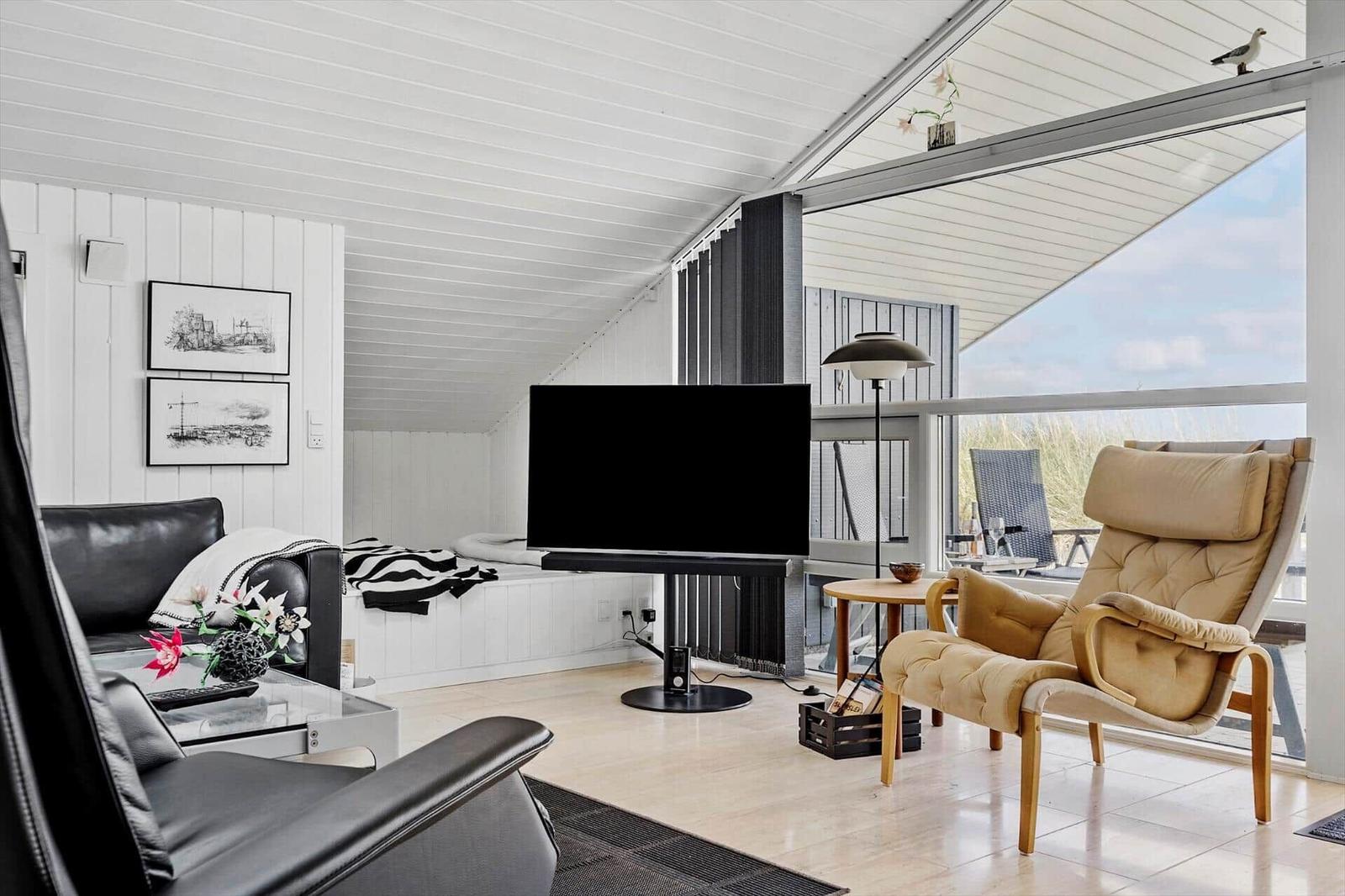 Wohnzimmer mit Sofa, Sessel und TV. Große Glasfront mit Blick auf die Landschaft.