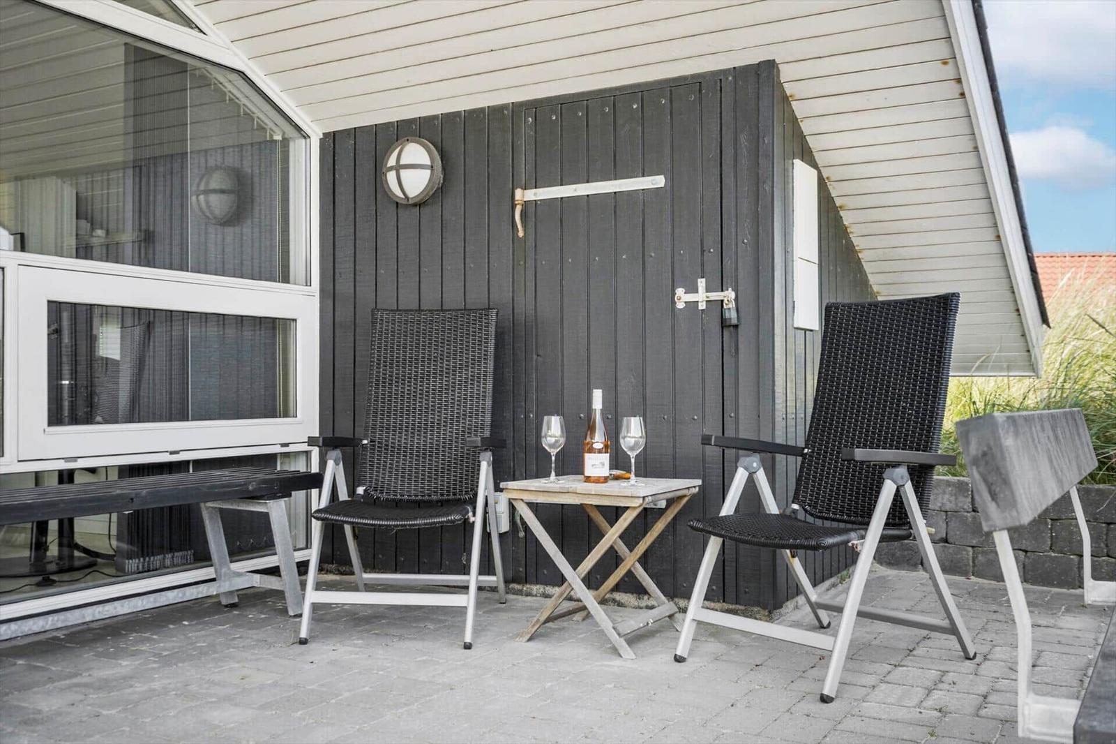 Terrasse mit zwei Stühlen, Tisch und Flasche. Hintergrund: Hauswand und Fenster.