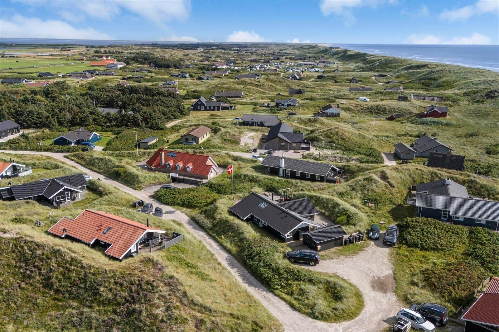 Aerielansicht von Häusern auf grünen Dünen mit Blick aufs Meer.