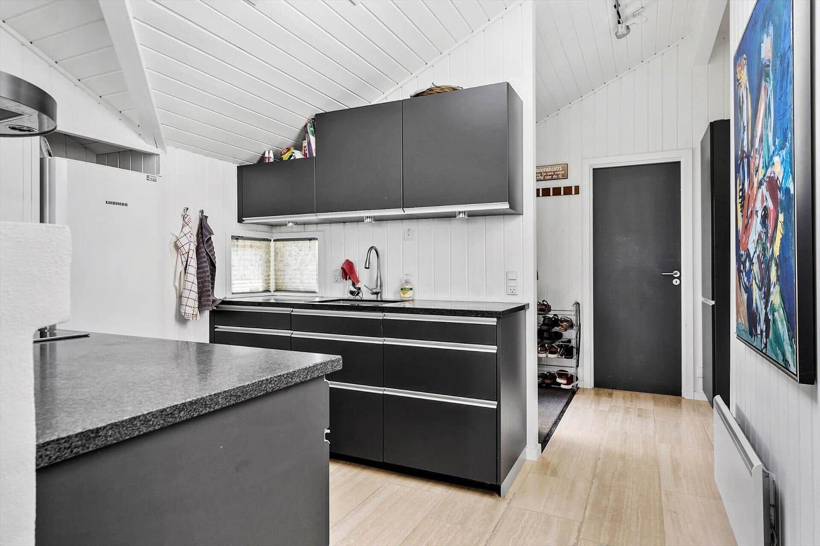Küche mit schwarzen Schränken, Arbeitsplatte und Spüle. Hintergrund: Flur mit Tür und Schuhregal.