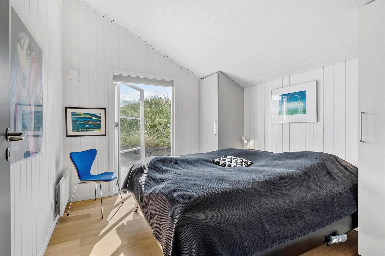 Schlafzimmer mit Bett, blauer Stuhl und Blick auf Grasflächen.