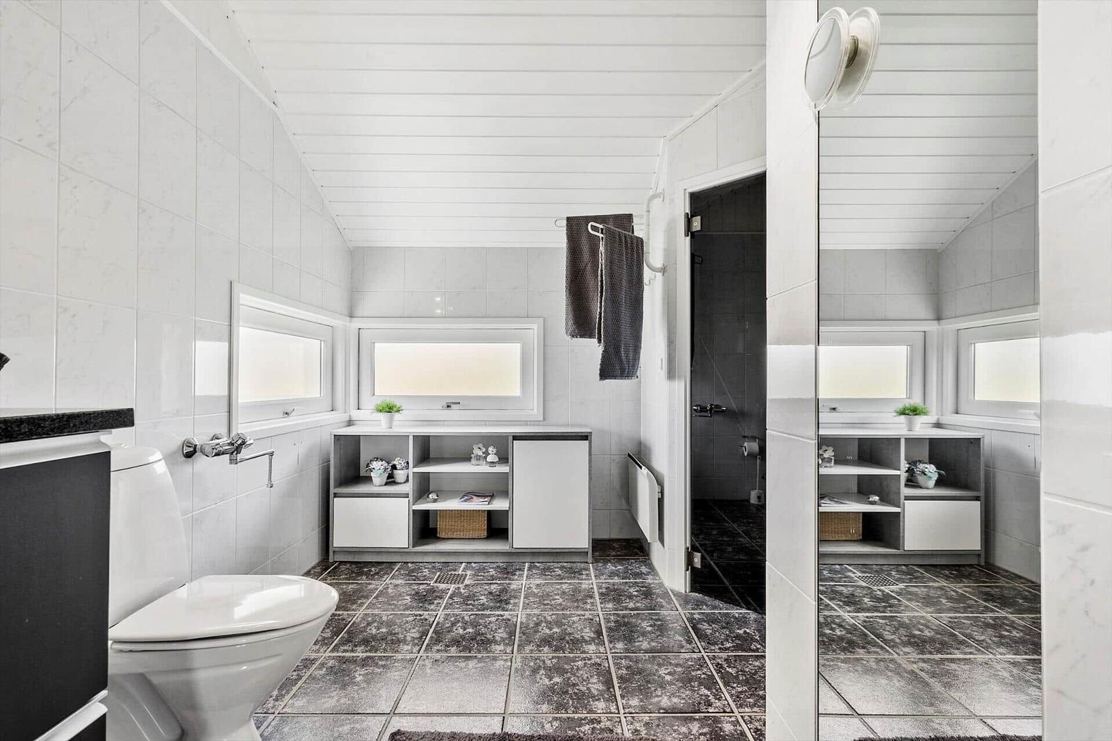 Badezimmer mit Toilette, Waschbecken und Dusche. Weiße Wände und dunkle Fliesen.