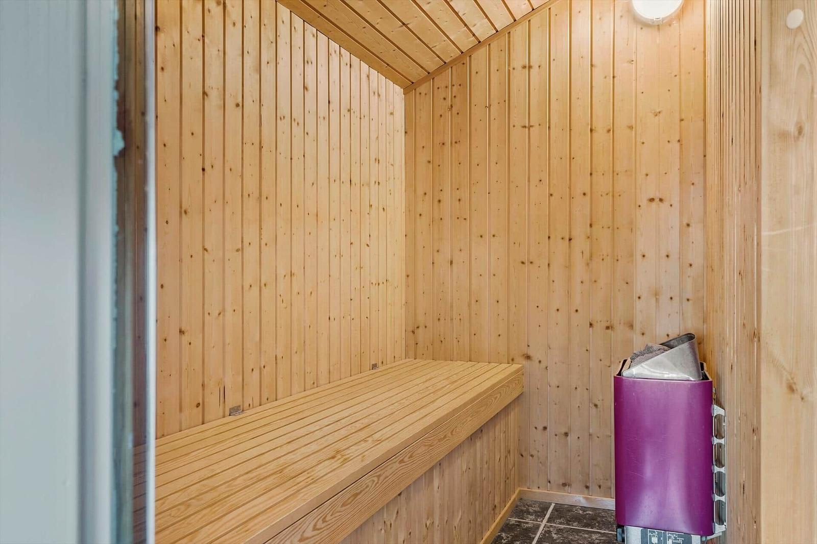 Sauna mit Holzwandverkleidung und Sitzbank. Ecke mit lila Mülltonne.