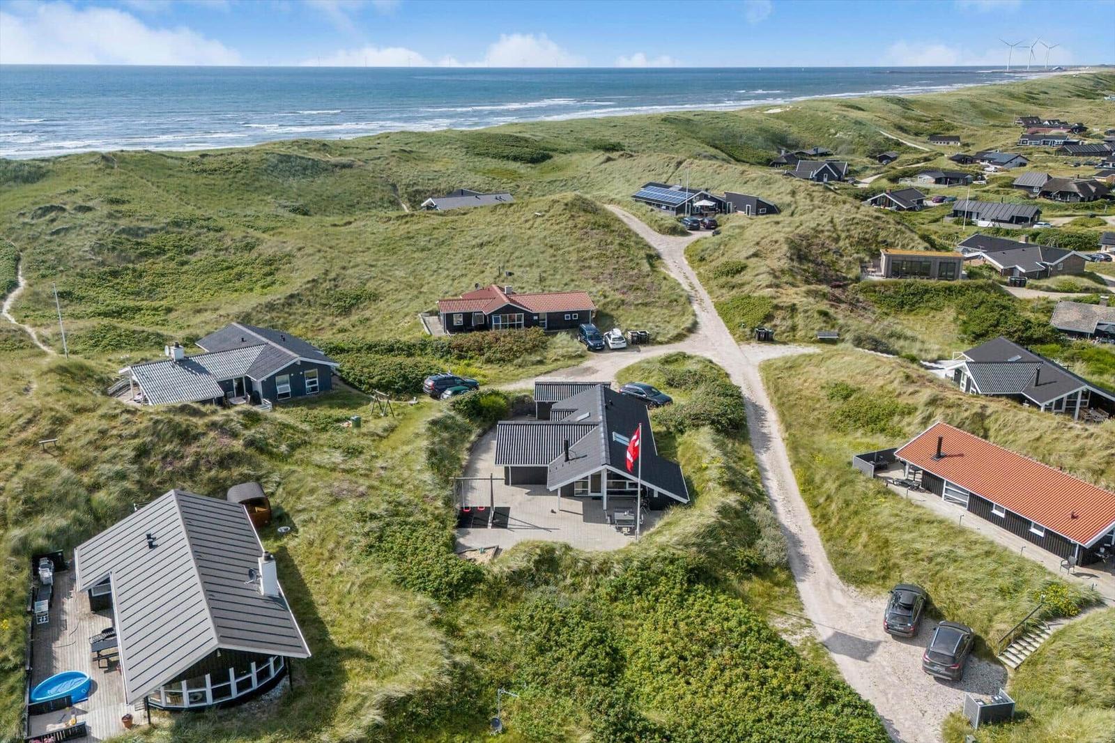 Meerblick auf grüne Dünen mit mehreren Ferienhäusern und einem sandigen Weg.