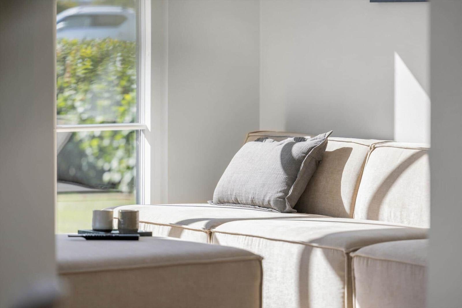 Ein Sofa mit Kissen und einem Beistelltisch vor einem Fenster mit Blick auf Grün.