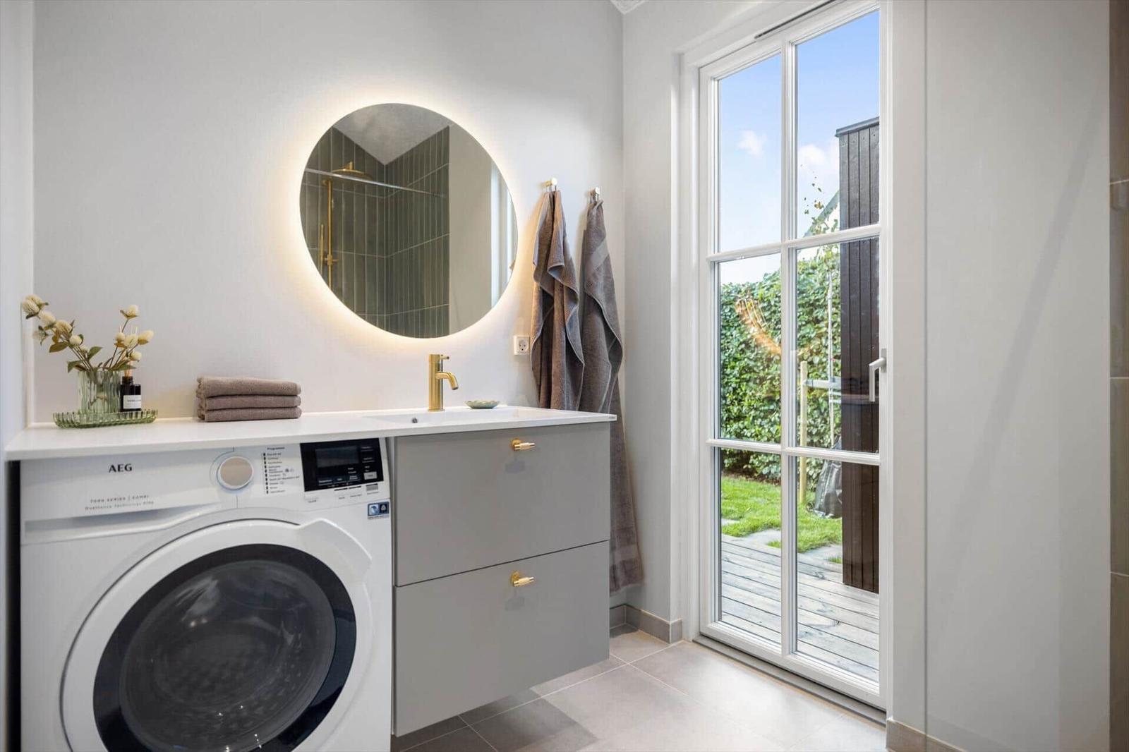 Badezimmer mit Waschmaschine, Spiegelschrank und Glastür zum Garten.
