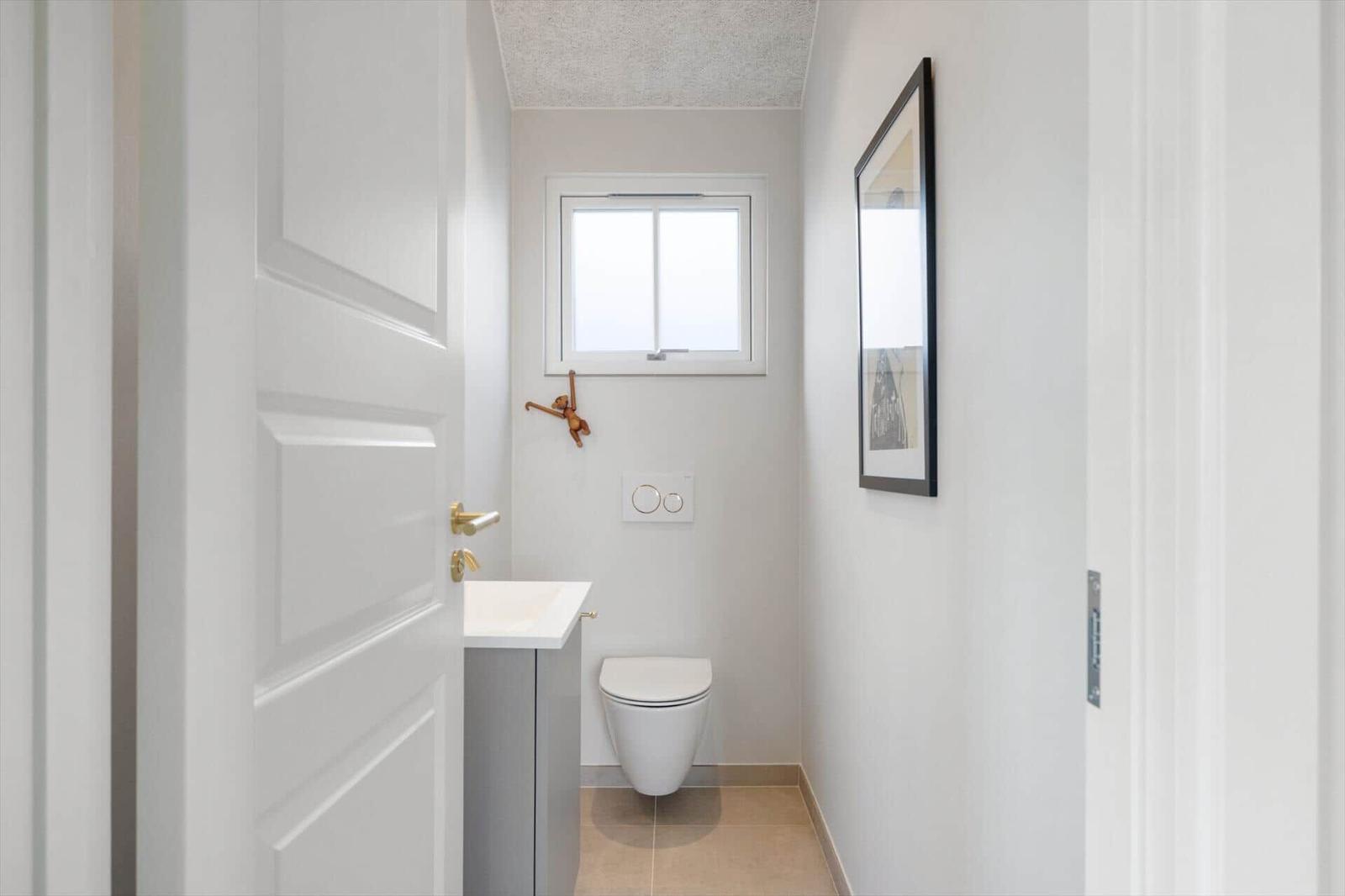 Badezimmer mit Toilette, Waschbecken und Fenster. Wandbild und Holzdekoration.