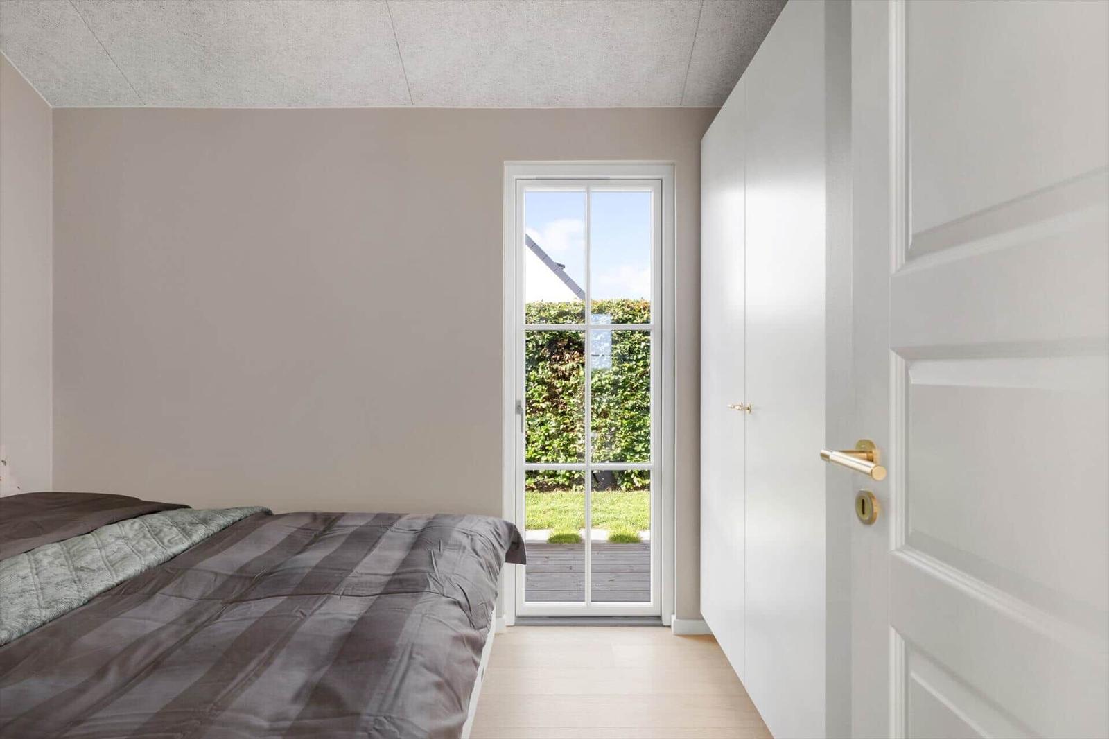 Schlafzimmer mit Bett, weißen Schränken und Tür zum Garten.
