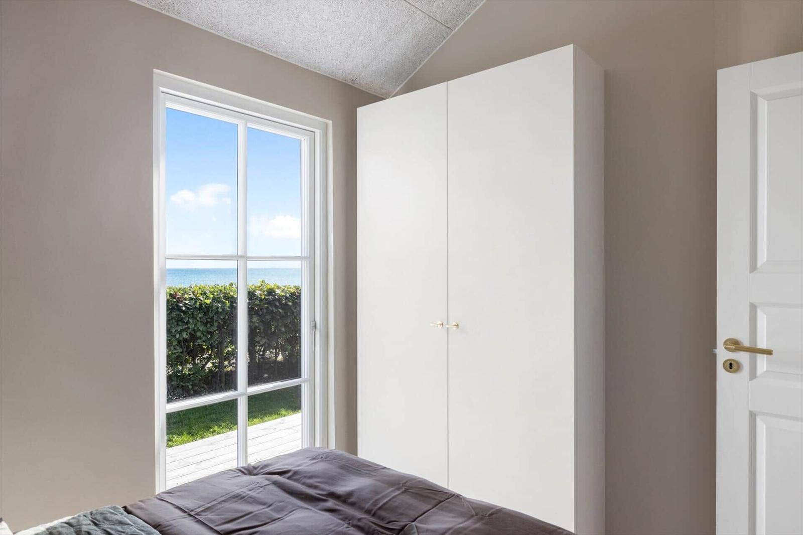 Schlafzimmer mit Blick auf Meer, weißer Schrank und Tür.