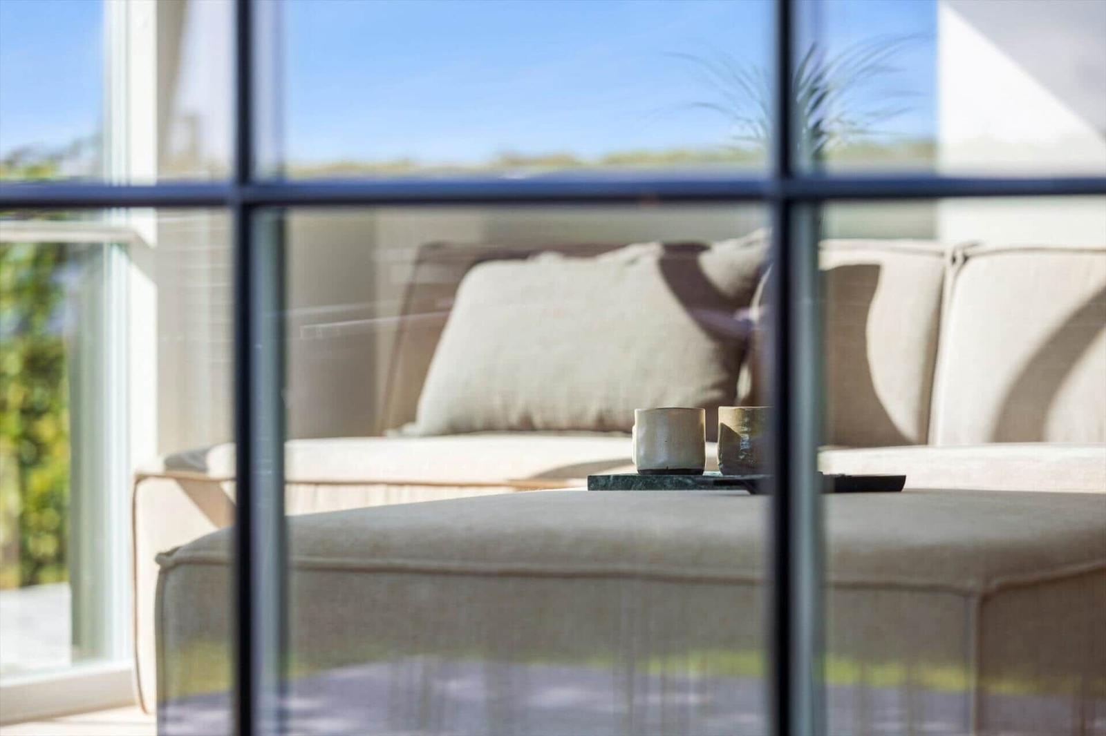 Durch Fenster sichtbarer Sitzbereich mit Sofa und Tisch mit Tassen.