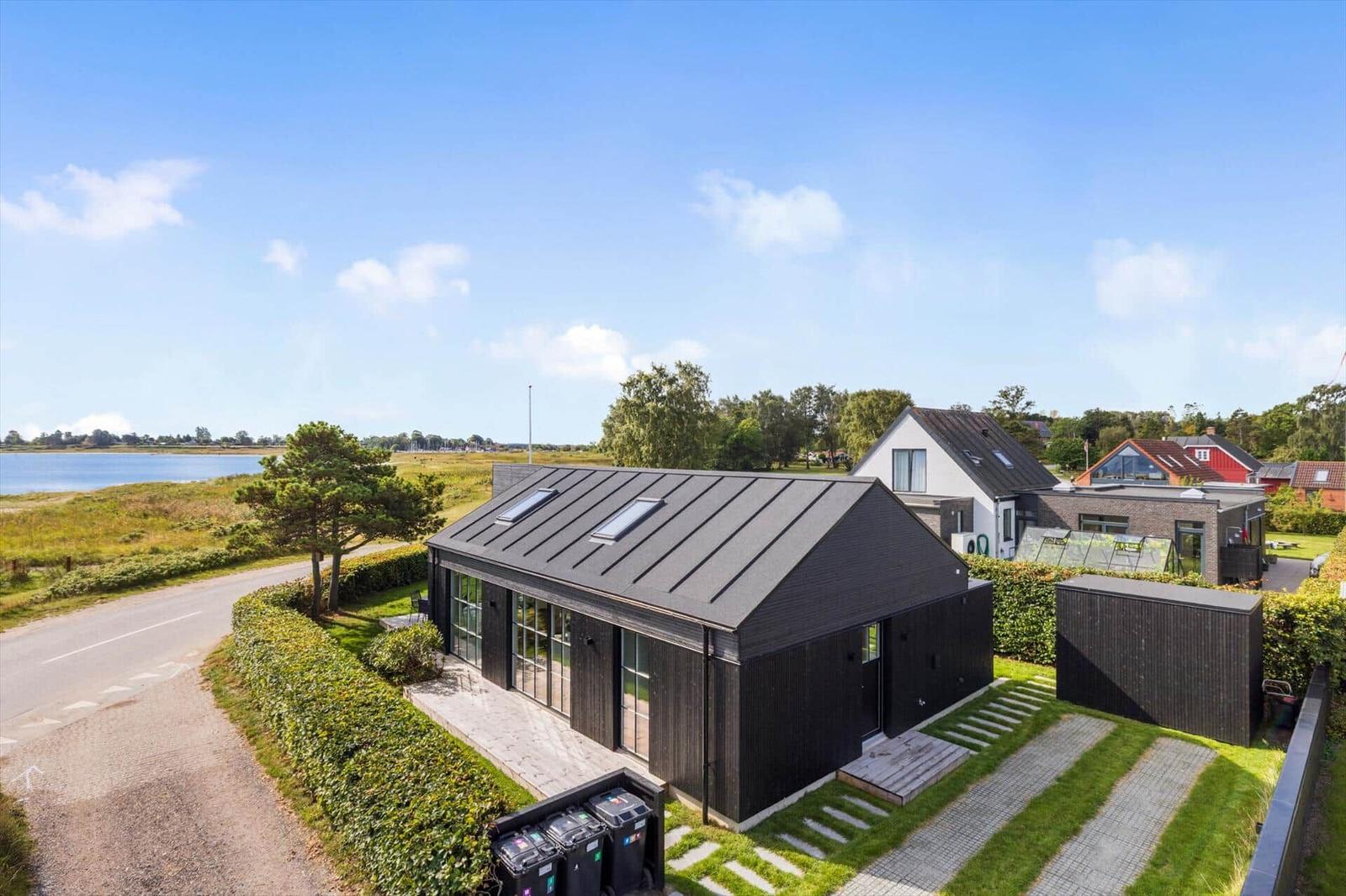 Moderne schwarze Villa mit großem Garten und Blick auf Wasser.