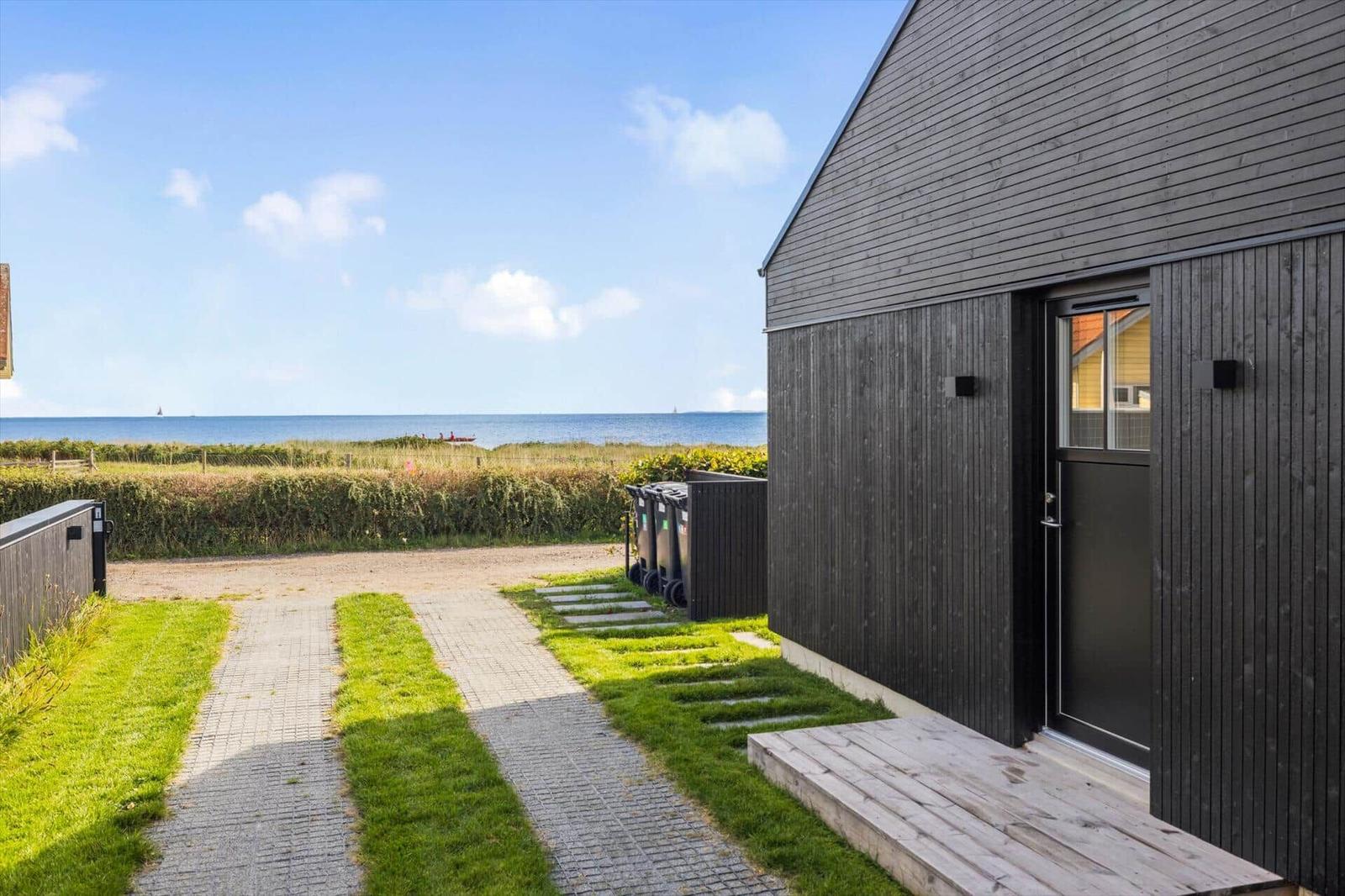 Haus mit Holzfassade und Eingangstür. Blick auf das Meer und einen Weg durch Gras.
