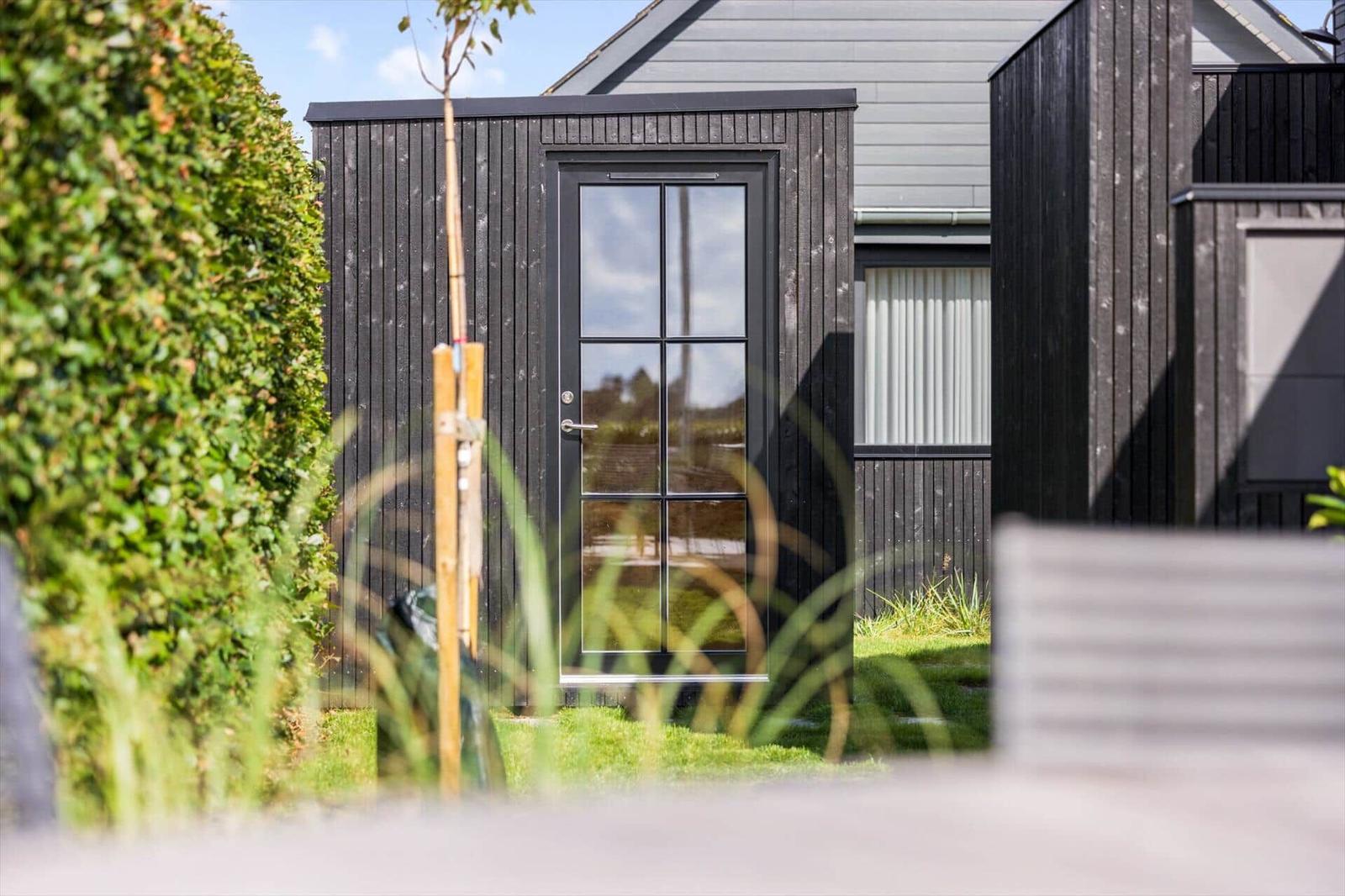 Schwarze Holzhütte mit Glasfront und Garten. Moderne Architektur im Freien.