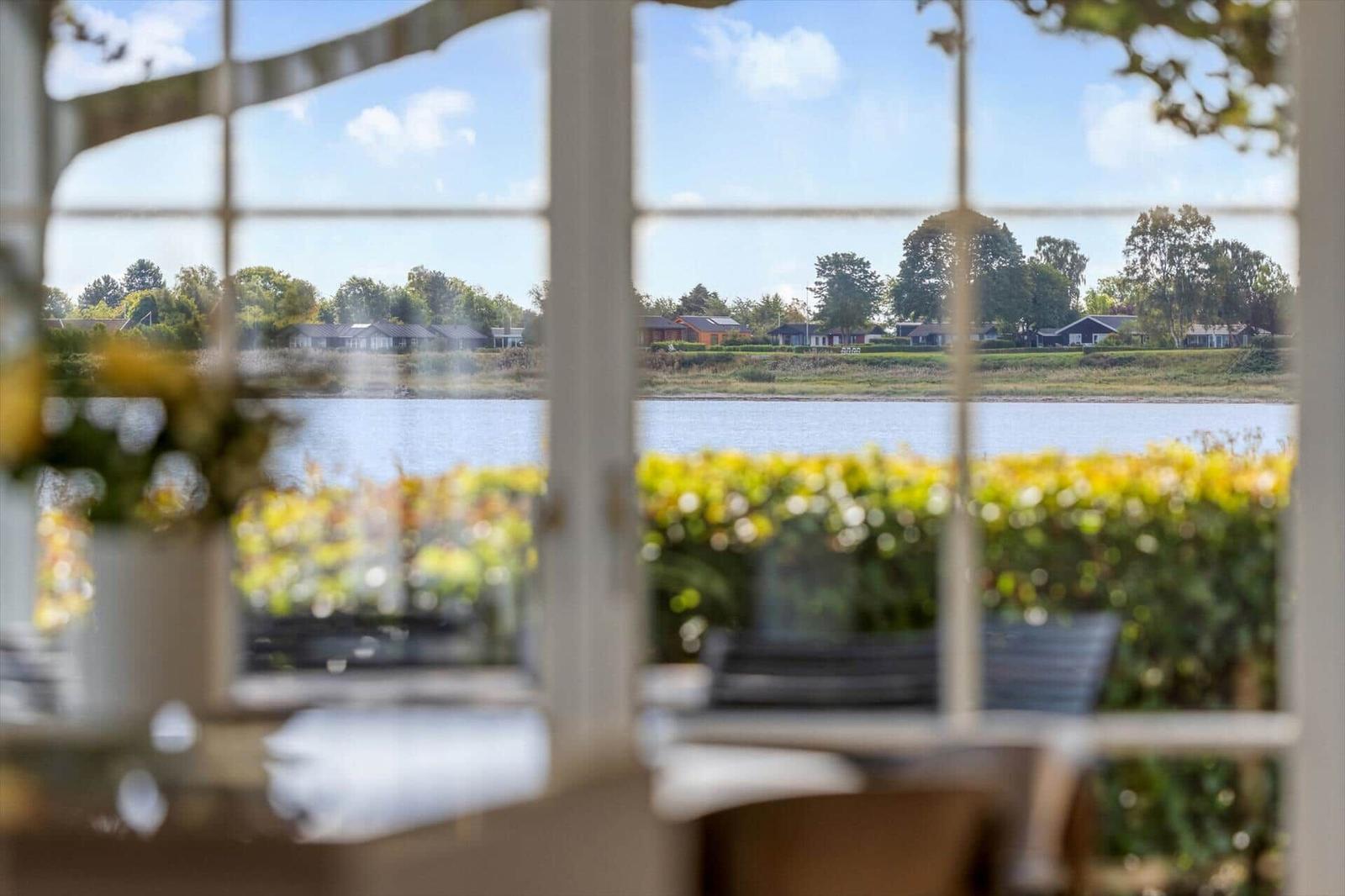 Durch ein Fenster blickt man auf einen See mit Uferhäusern und Bäumen.