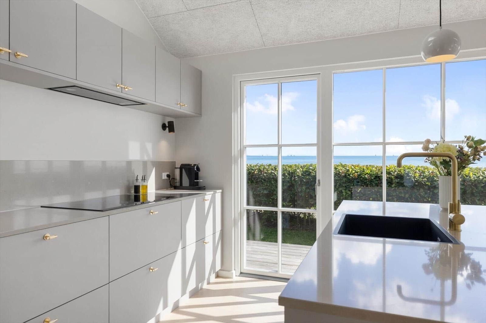 Moderne Küche mit Blick auf den Ozean und grüne Hecke. Edle Oberflächen und goldene Griffe.