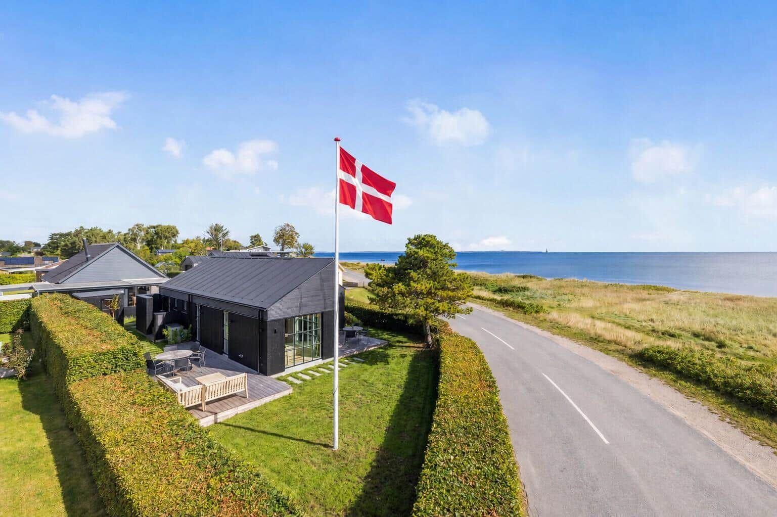 Moderne Villa mit Terrasse, Flagge und Meerblick. Grünhedge und asphaltierter Weg.