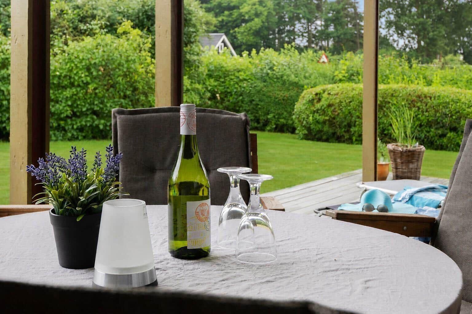 Tisch mit Weinglas, Flasche und Pflanze im Freien mit Blick auf Garten.